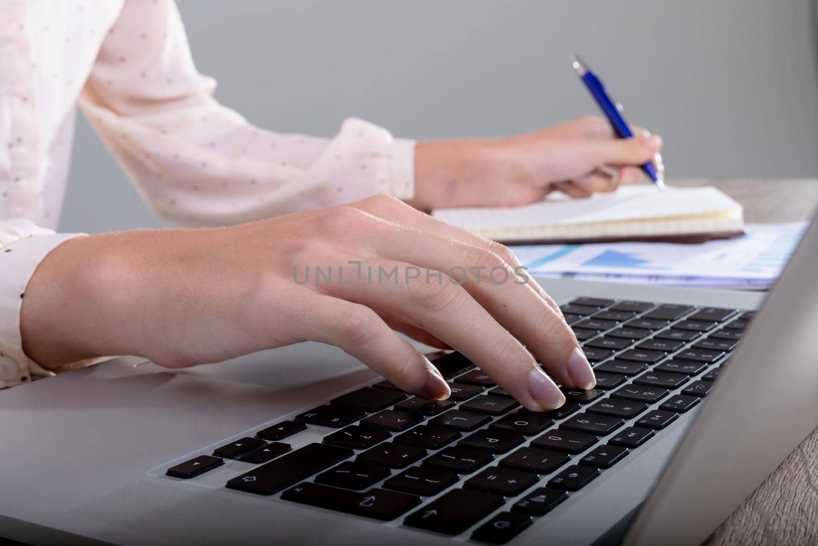 Midsection of caucasian businesswoman using laptop and taking notes, isolated on grey background by Wavebreakmedia
