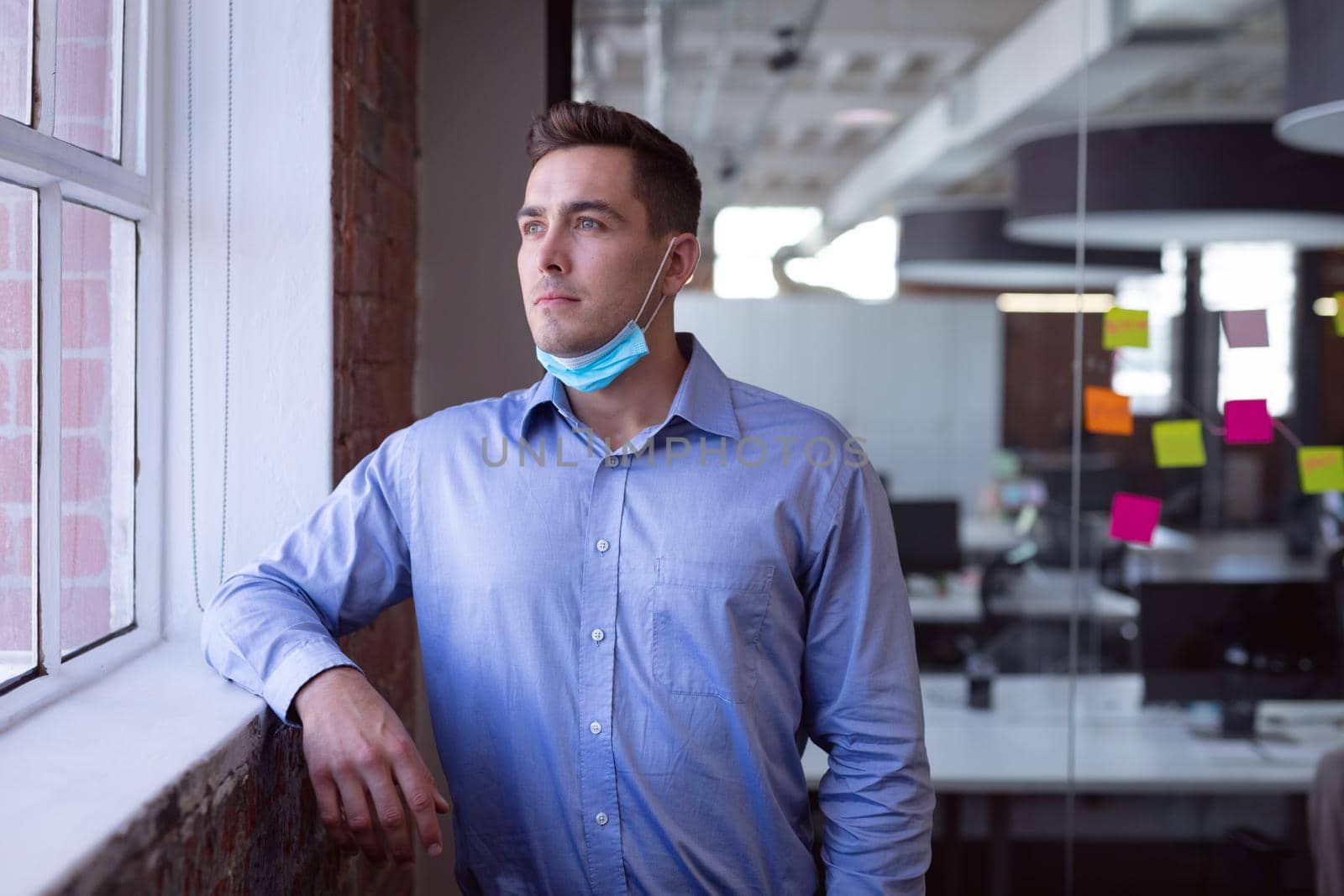 Portrait of thoughtful caucasian businessman in lowered face mask looking out of window by Wavebreakmedia