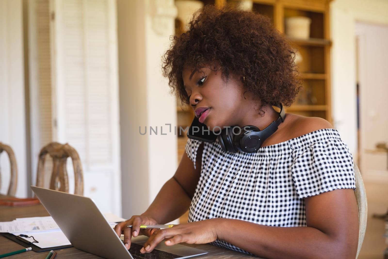 African american woman working in living room using laptop and talking on smartphone. technology and communication, flexible working from home.