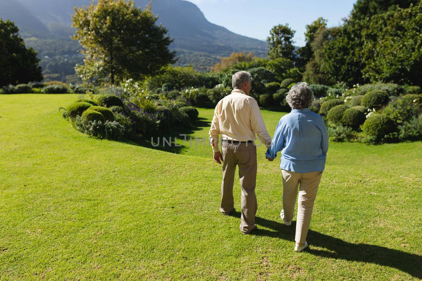 Senior caucasian couple walking together in sunny garden. retreat, retirement and happy senior lifestyle concept.