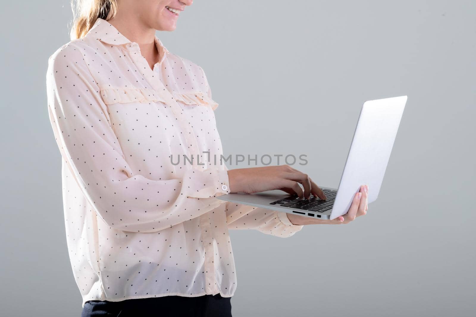 Smiling caucasian businesswoman using laptop, isolated on grey background by Wavebreakmedia