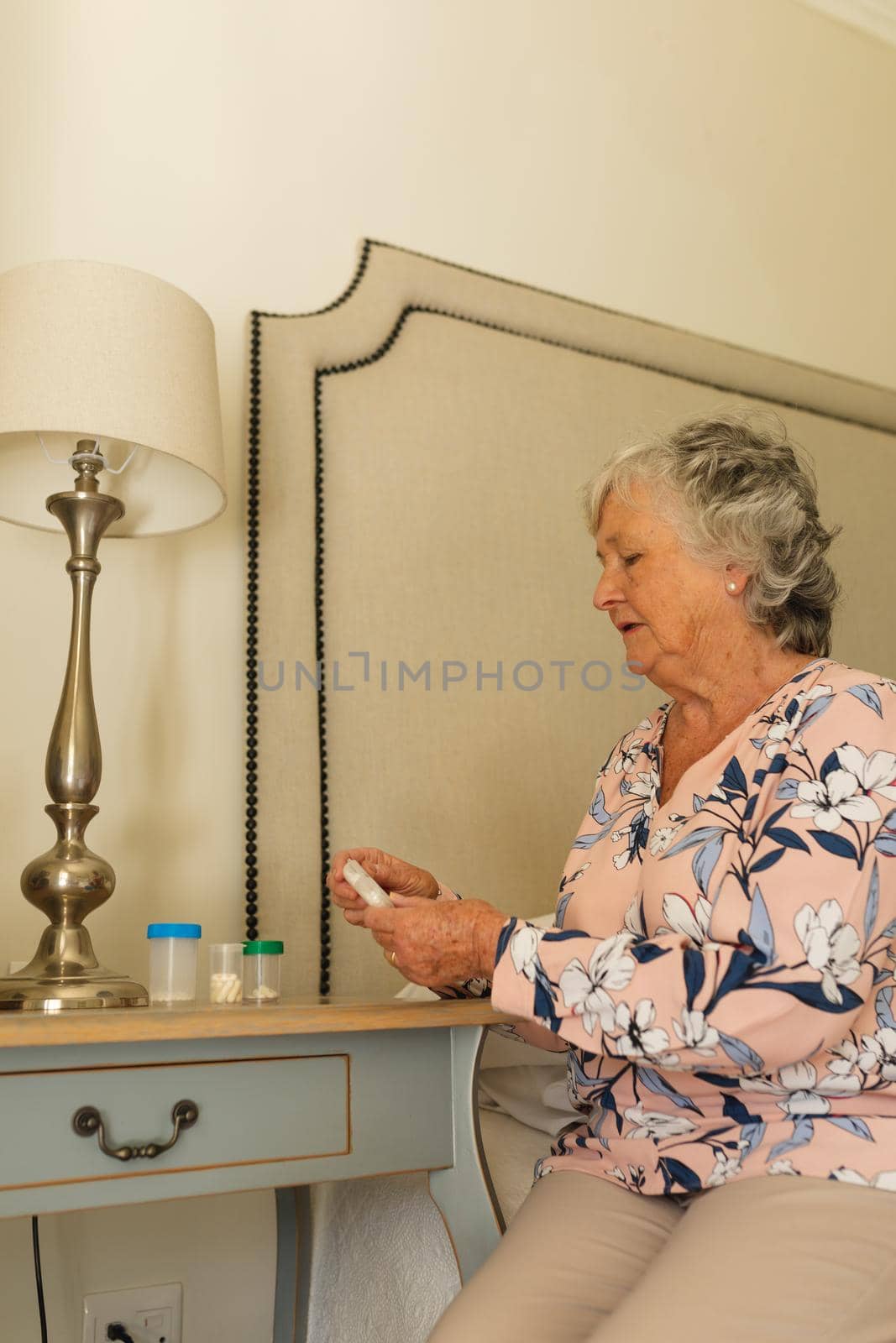 Senior caucasian woman sitting on bed holding box of pills. retreat, retirement and senior lifestyle concept.