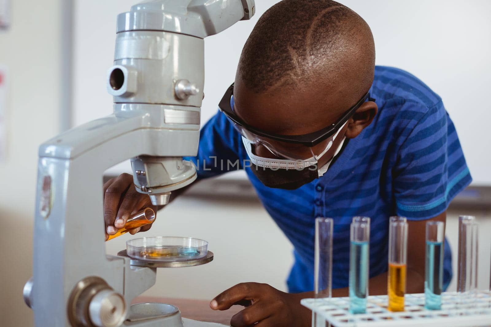 African american schoolboy in safety glasses and face mask using microscope in science class by Wavebreakmedia