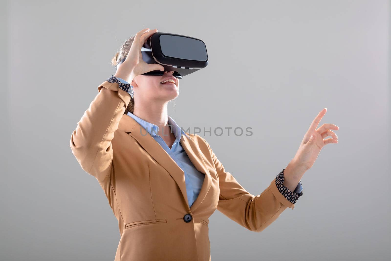 Caucasian businesswoman wearing vr headset touching virtual interface, isolated on grey background. business, technology, communication and growth concept.