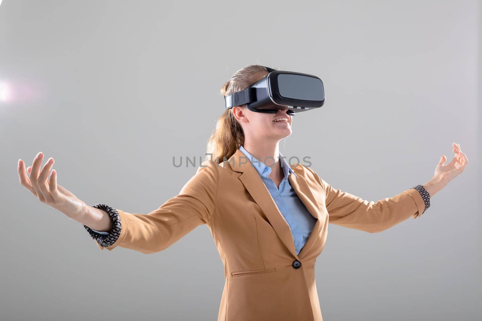 Caucasian businesswoman wearing vr headset widening her arms, isolated on grey background by Wavebreakmedia