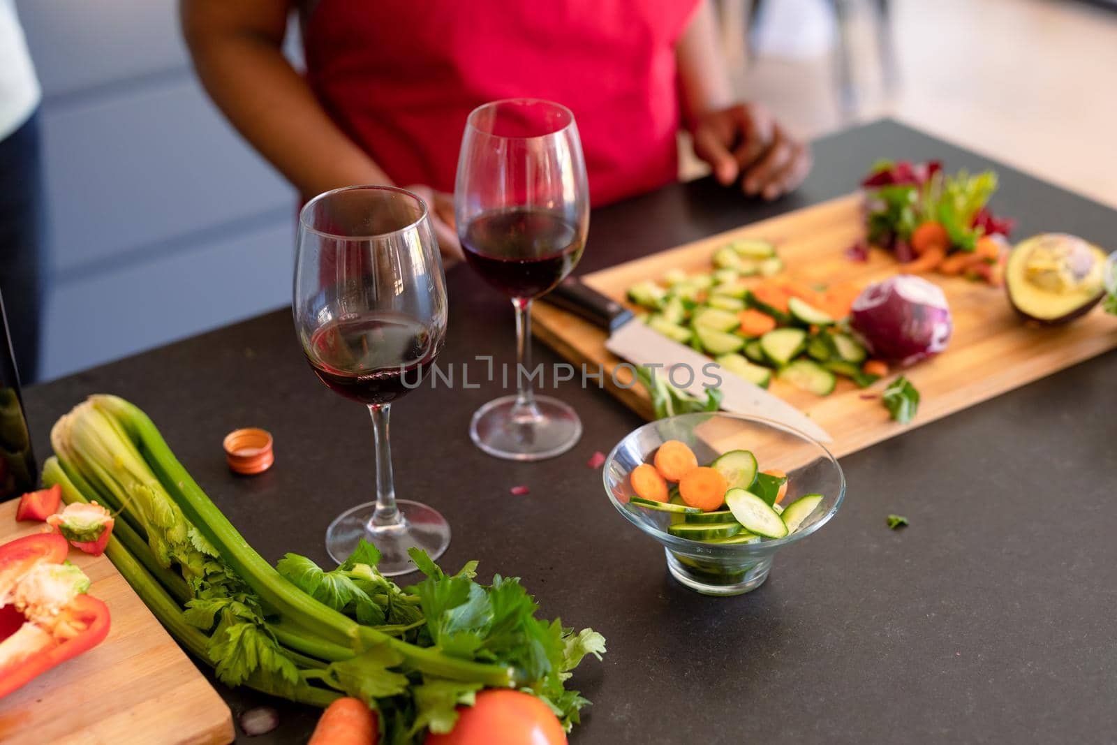 Two glasses with red wine on kitchen table, african american senior woman in background by Wavebreakmedia