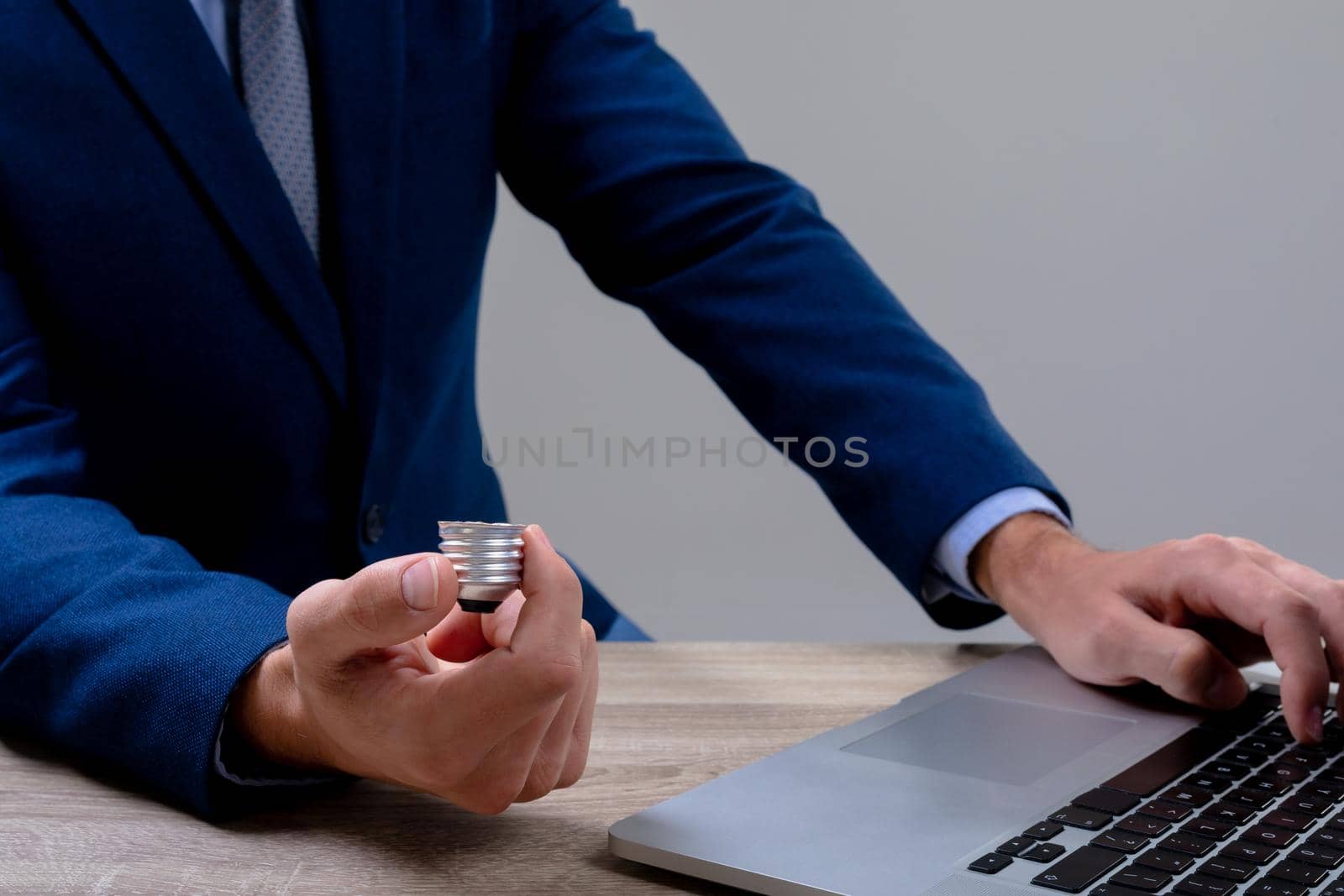 Midsection of caucasian businessman holding base of light bulb, isolated on grey background. business technology, communication and growth concept.