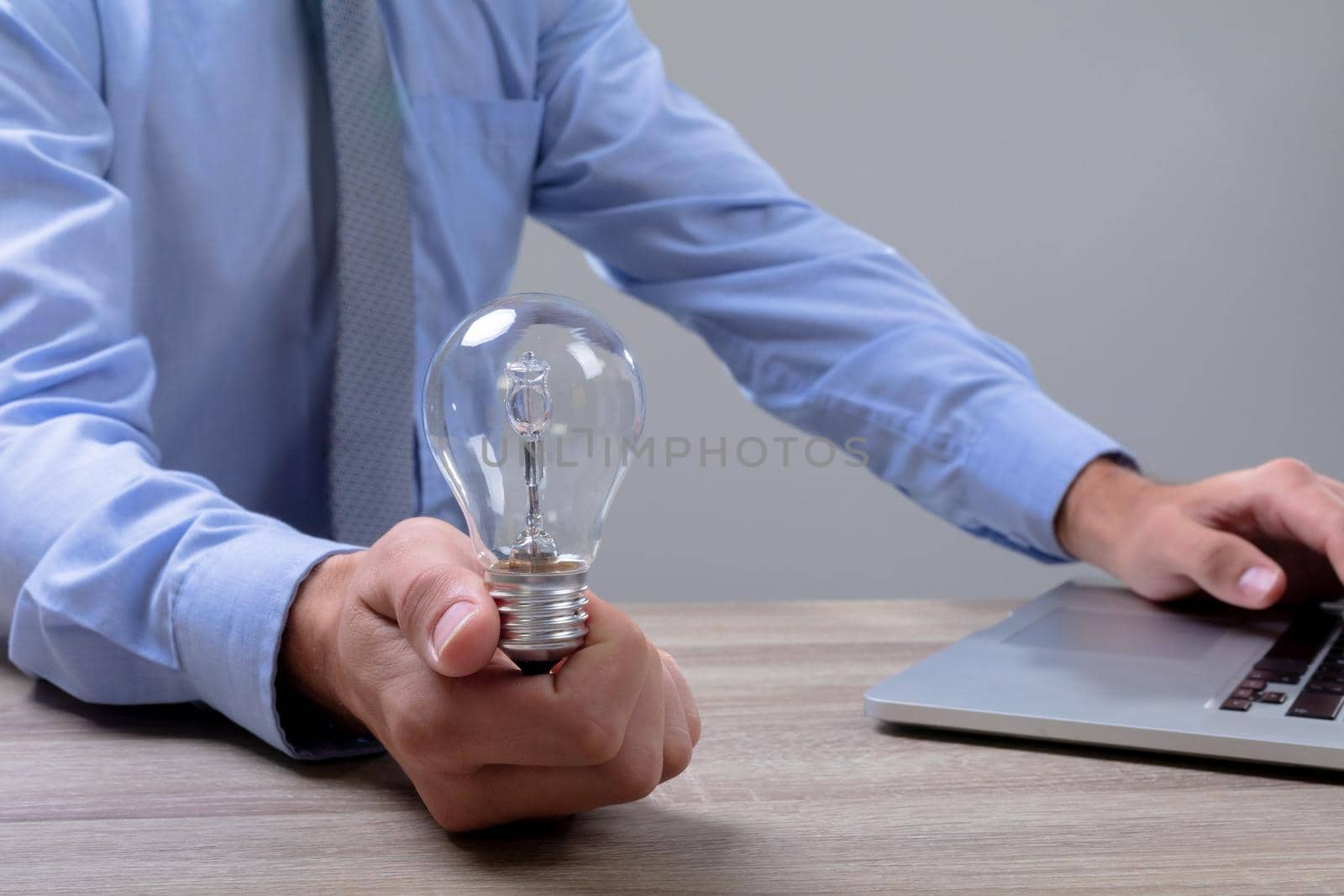 Midsection of caucasian businessman holding light bulb using laptop, isolated on grey background. business technology, communication and growth concept.