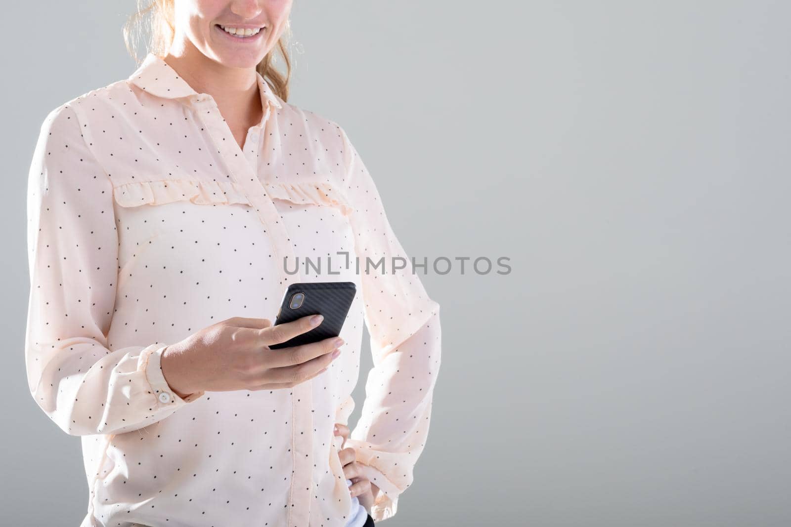 Smiling caucasian businesswoman using smartphone, isolated on grey background by Wavebreakmedia