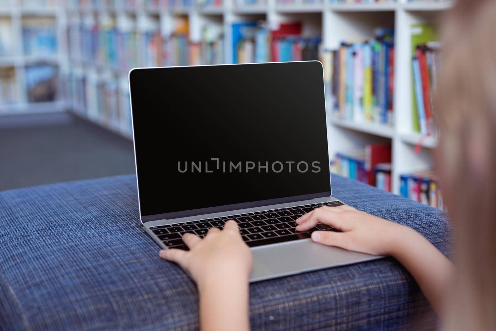 Caucasian schoolgirl at desk in school library using laptop, with copy space on screen. childhood, technology and education at elementary school.