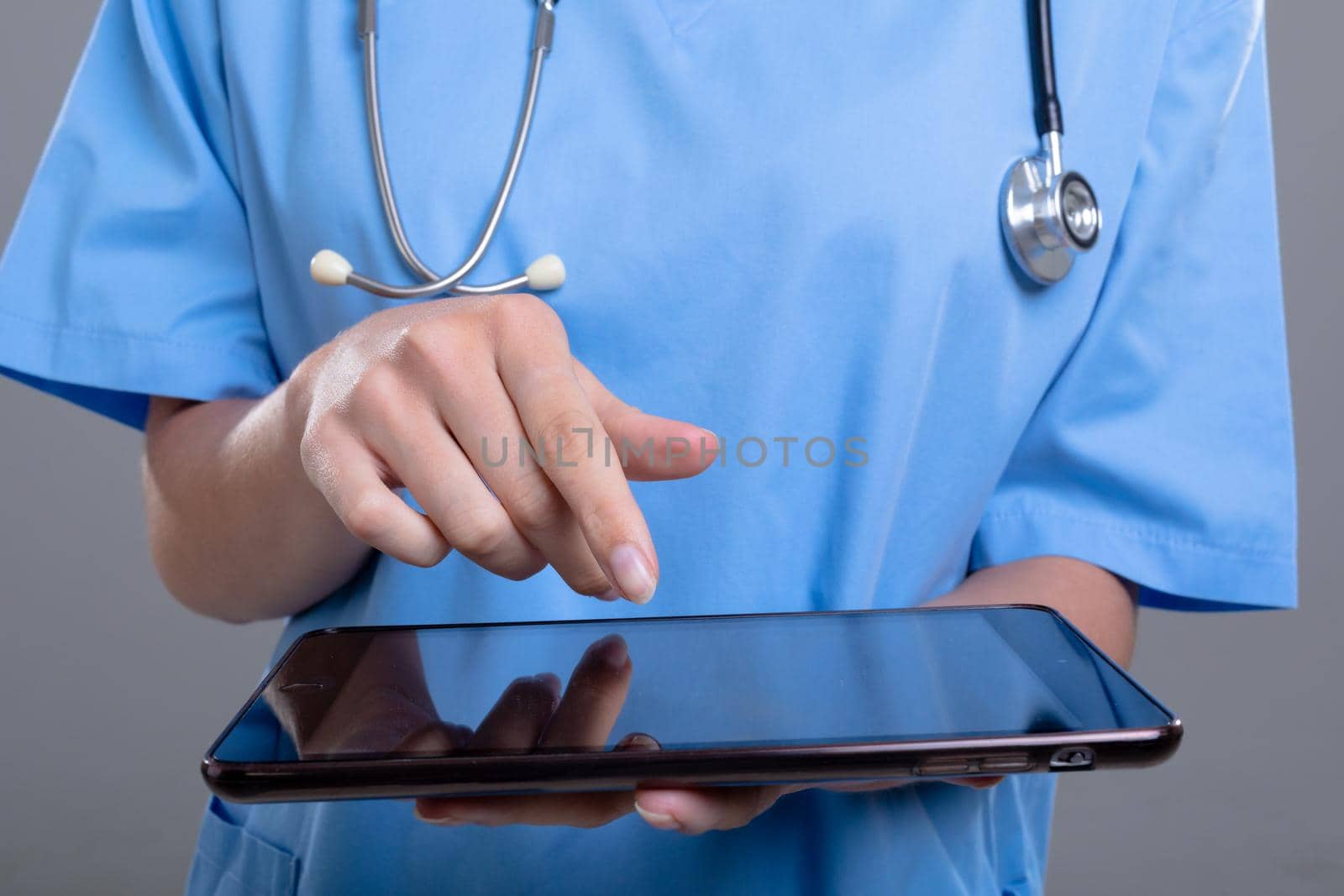 Midsection of caucasian female doctor using tablet, isolated on grey background. medical and healthcare services concept.