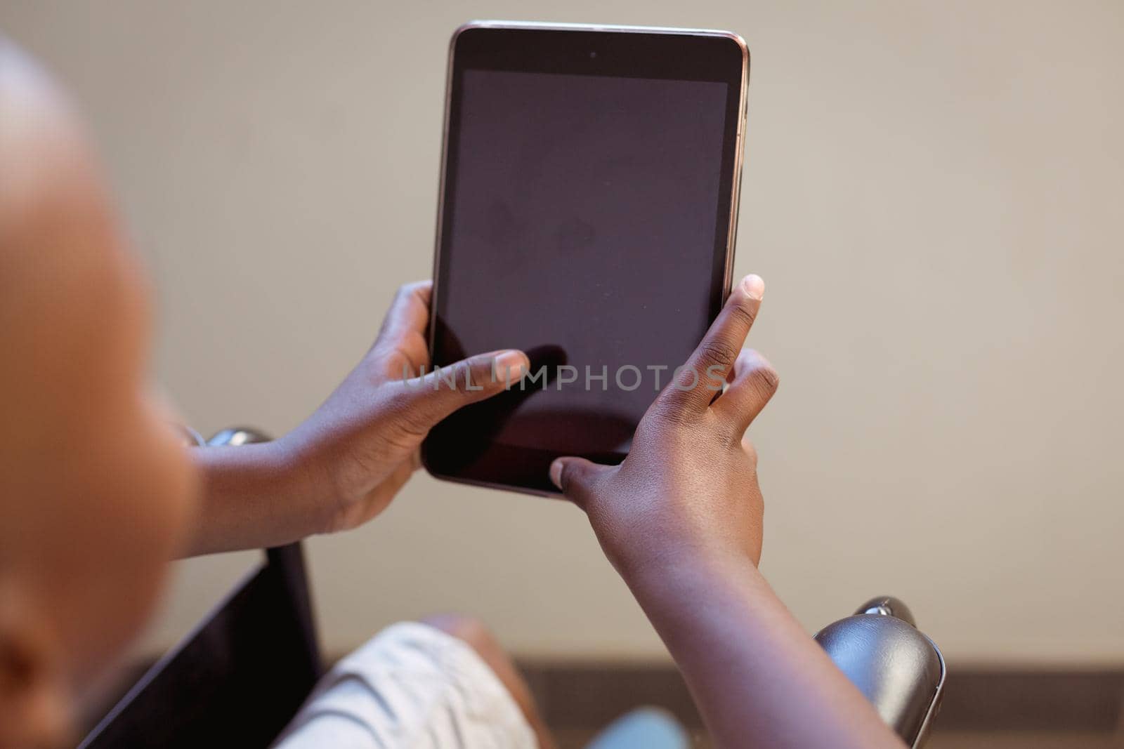 Disabled african american schoolboy sitting in wheelchair using tablet, copy space on screen. childhood, technology and education at elementary school. childhood and education at elementary school.