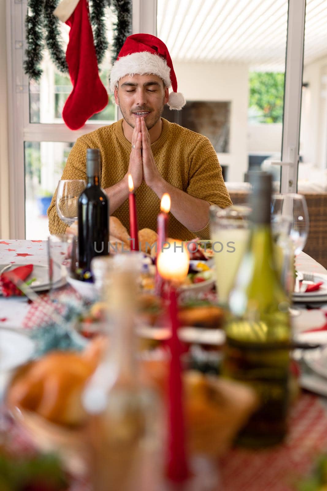 Caucasian man wearing santa hat praying at christmas table. family christmas time and festivity together at home.