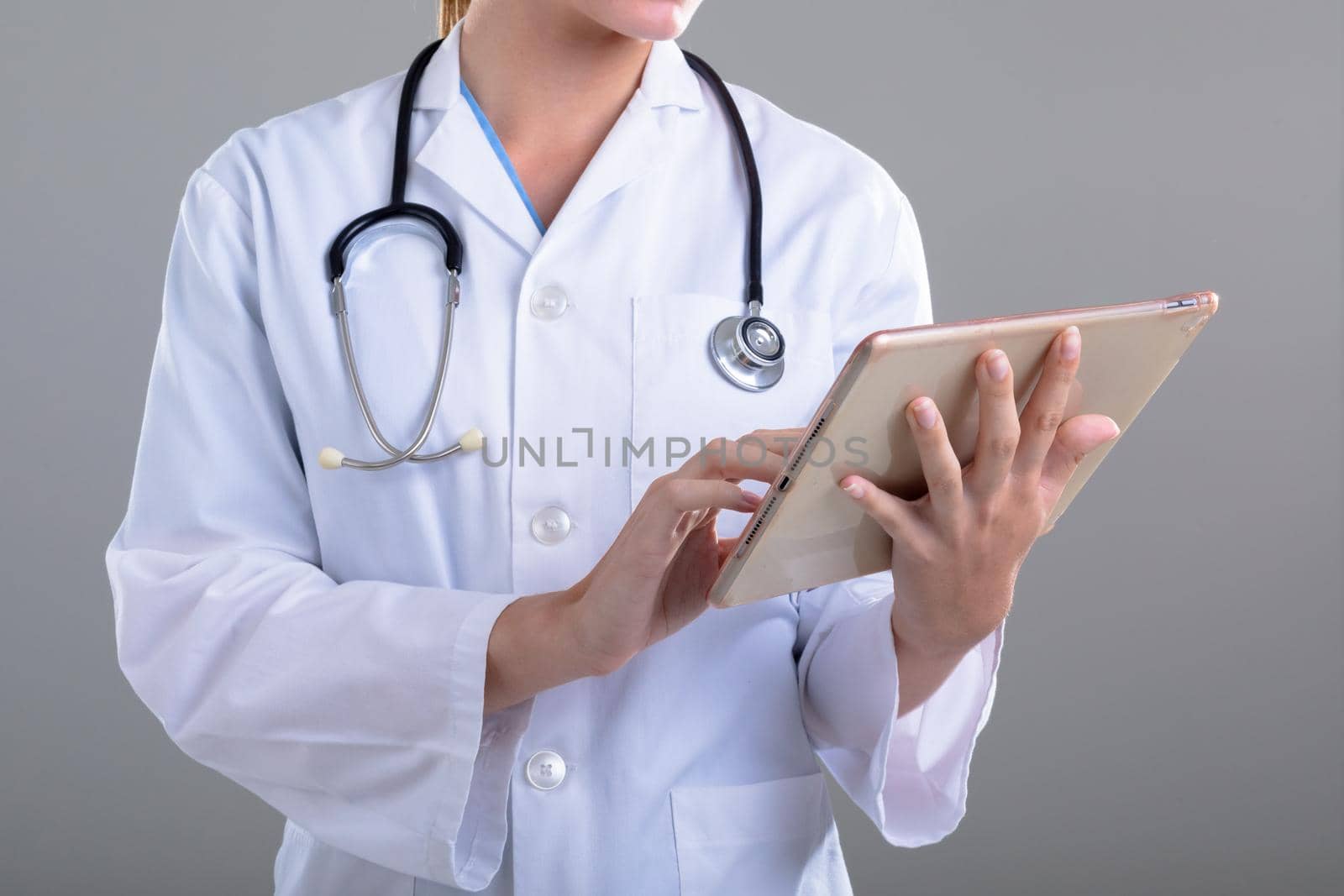 Midsection of caucasian female doctor using tablet, isolated on grey background. medical and healthcare services concept.