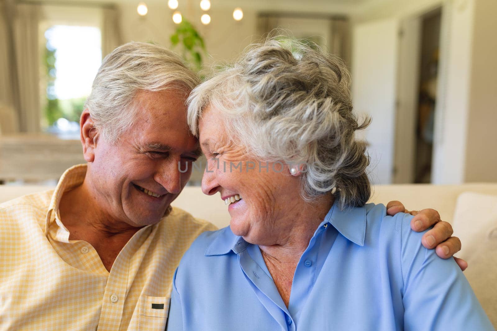 Senior caucasian couple sitting on sofa embracing and smiling. retreat, retirement and happy senior lifestyle concept.