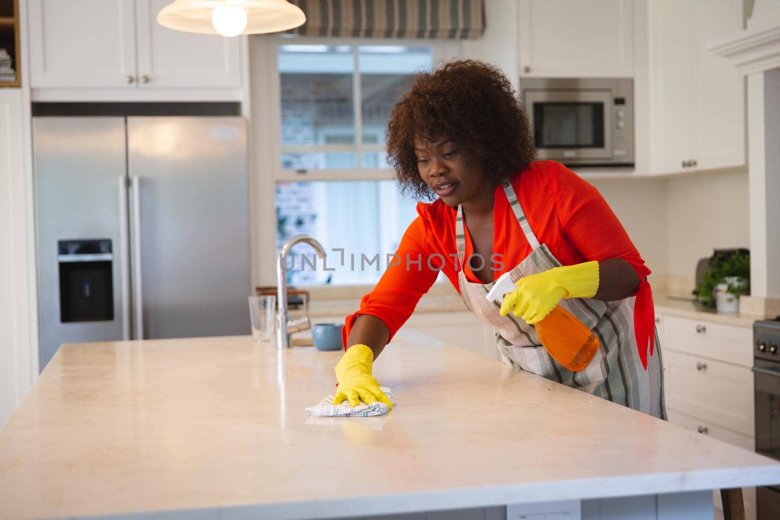 Happy african american woman in kitchen wearing rubber gloves, cleaning kitchen worktop. spending free time at home.