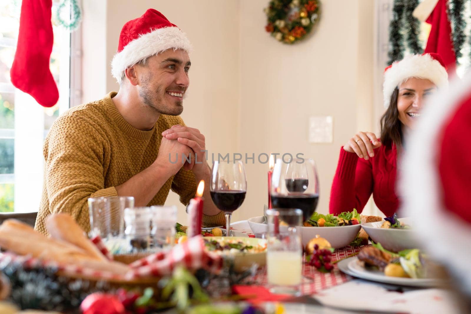 Happy caucasian couple wearing santa hats sitting at christmas table with family. family christmas time and festivity together at home.