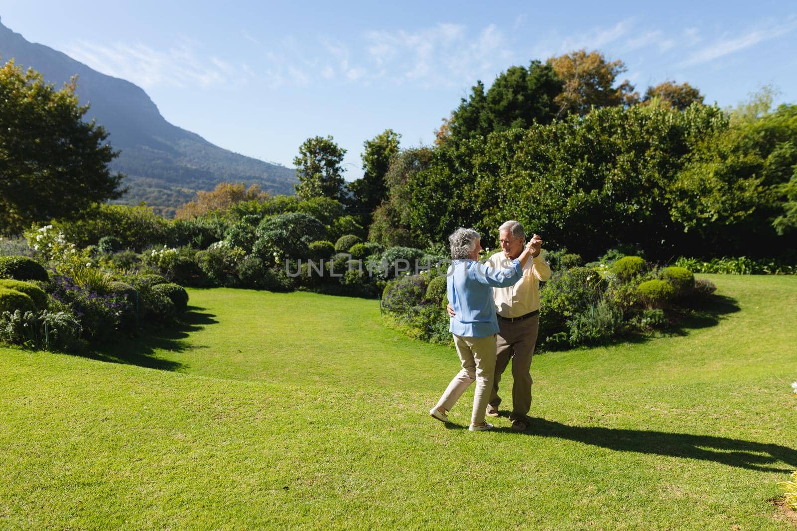 Senior caucasian couple dancing together in sunny garden. retreat, retirement and happy senior lifestyle concept.