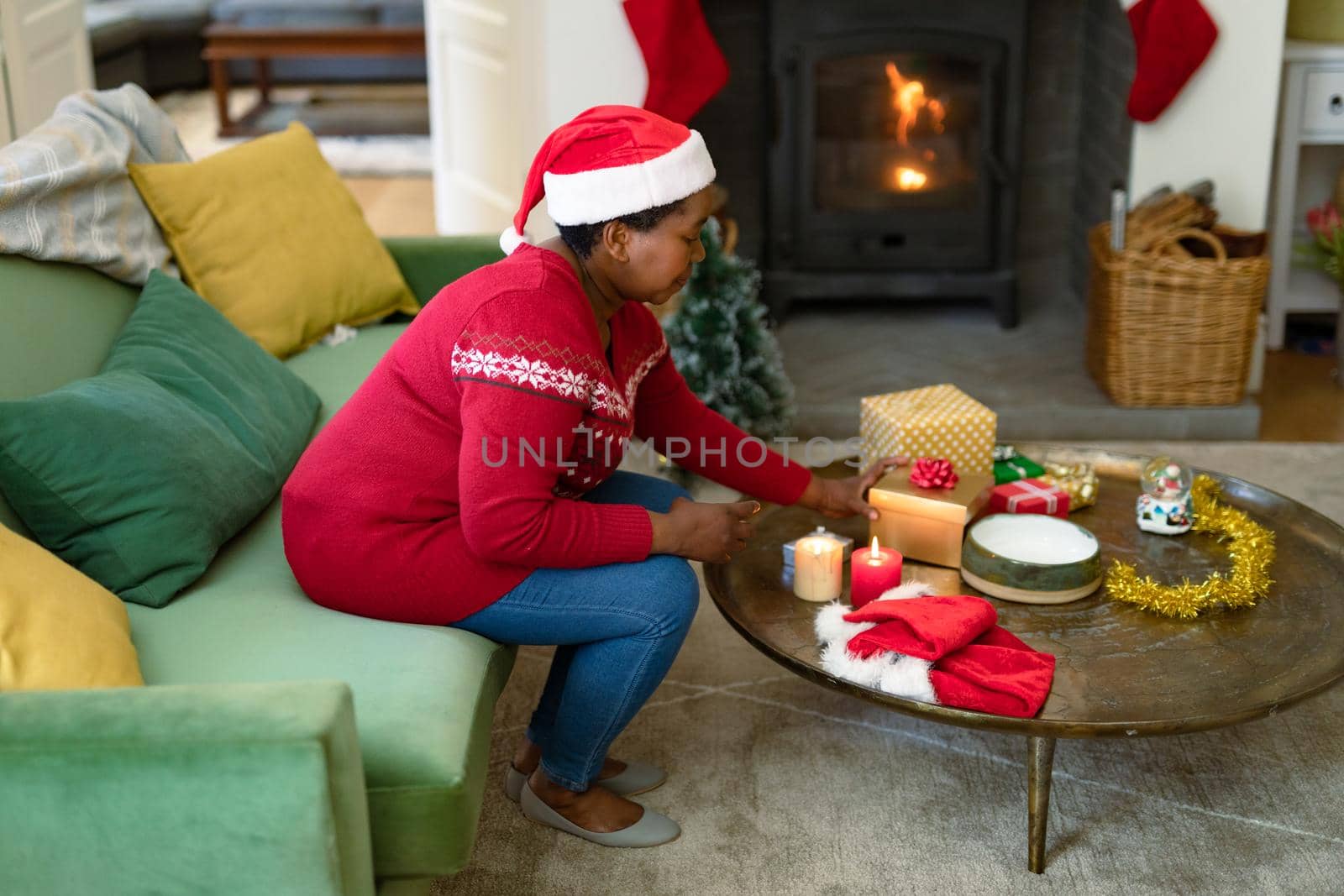African american senior woman in santa hat opening present at christmas time. retirement lifestyle and christmas festivities, celebrating at home.