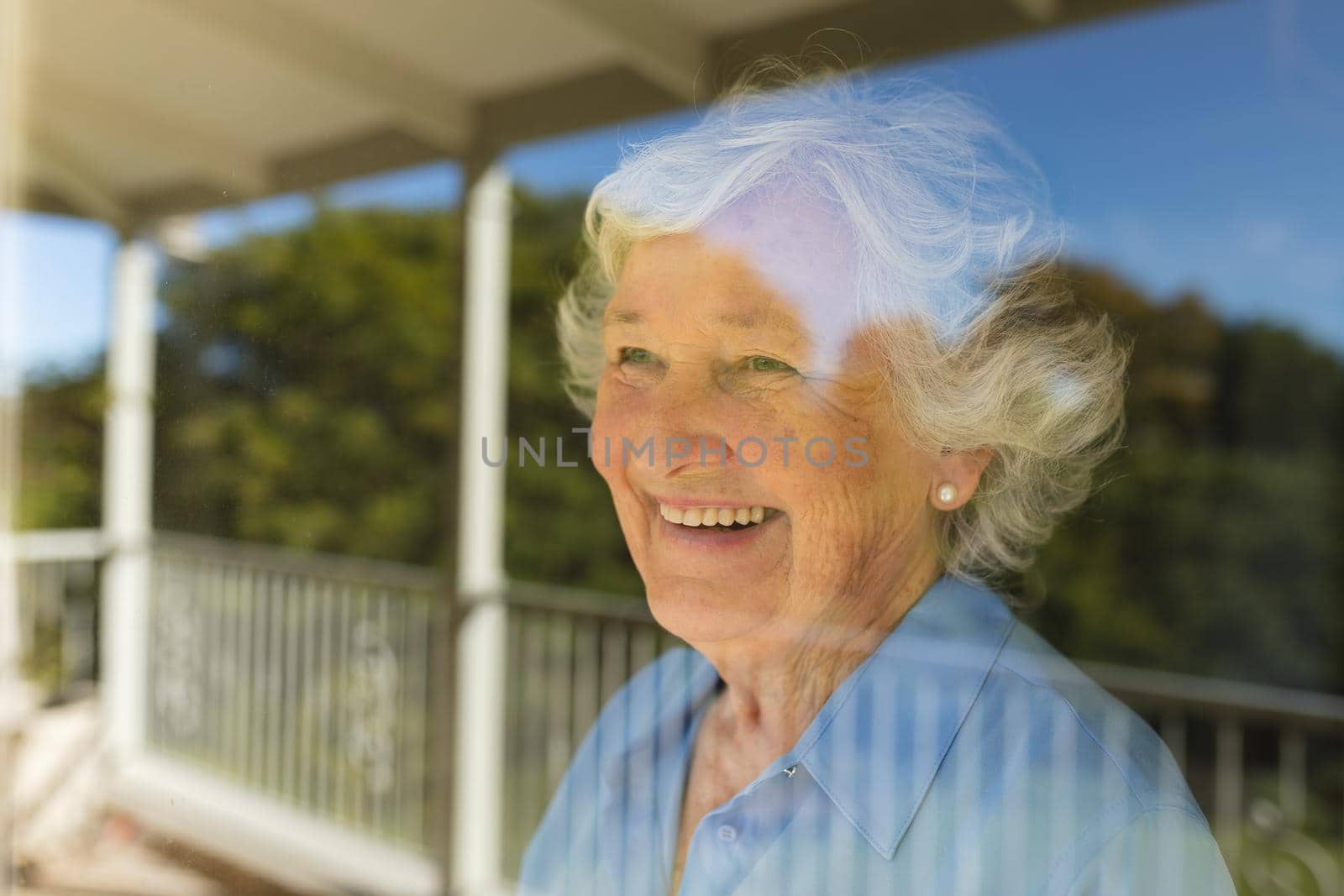 Senior caucasian woman looking through window and smiling. retreat, retirement and happy senior lifestyle concept.