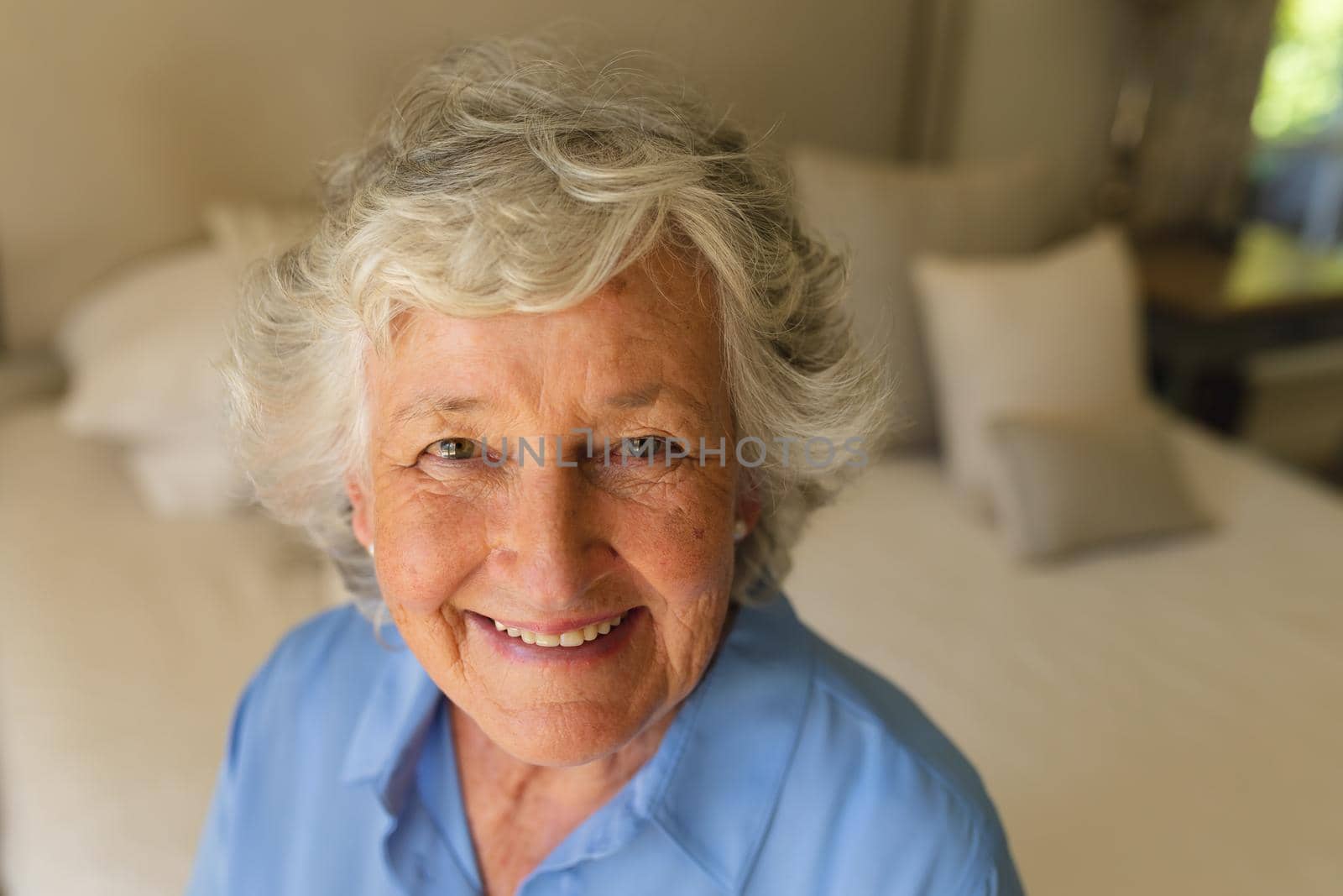 Portrait of senior caucasian woman sitting on bed and smiling in bedroom by Wavebreakmedia