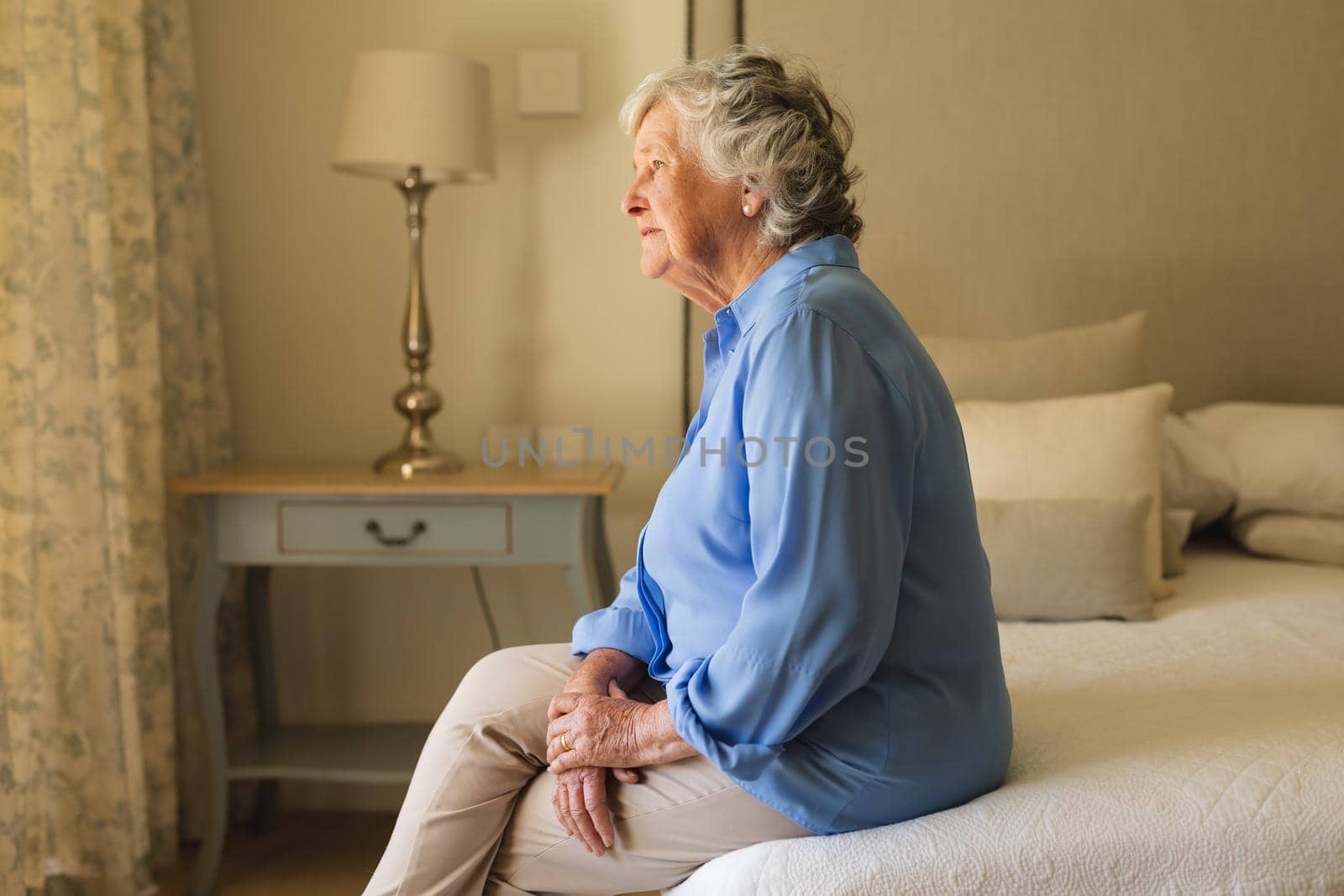 Senior caucasian woman sitting on bed and thinking in bedroom. retreat, retirement and senior lifestyle concept.