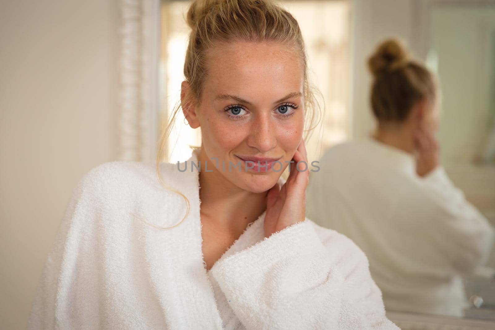 Portrait of smiling caucasian woman standing in bathroom wearing bathrobe. health, beauty and wellbeing, spending quality time at home.
