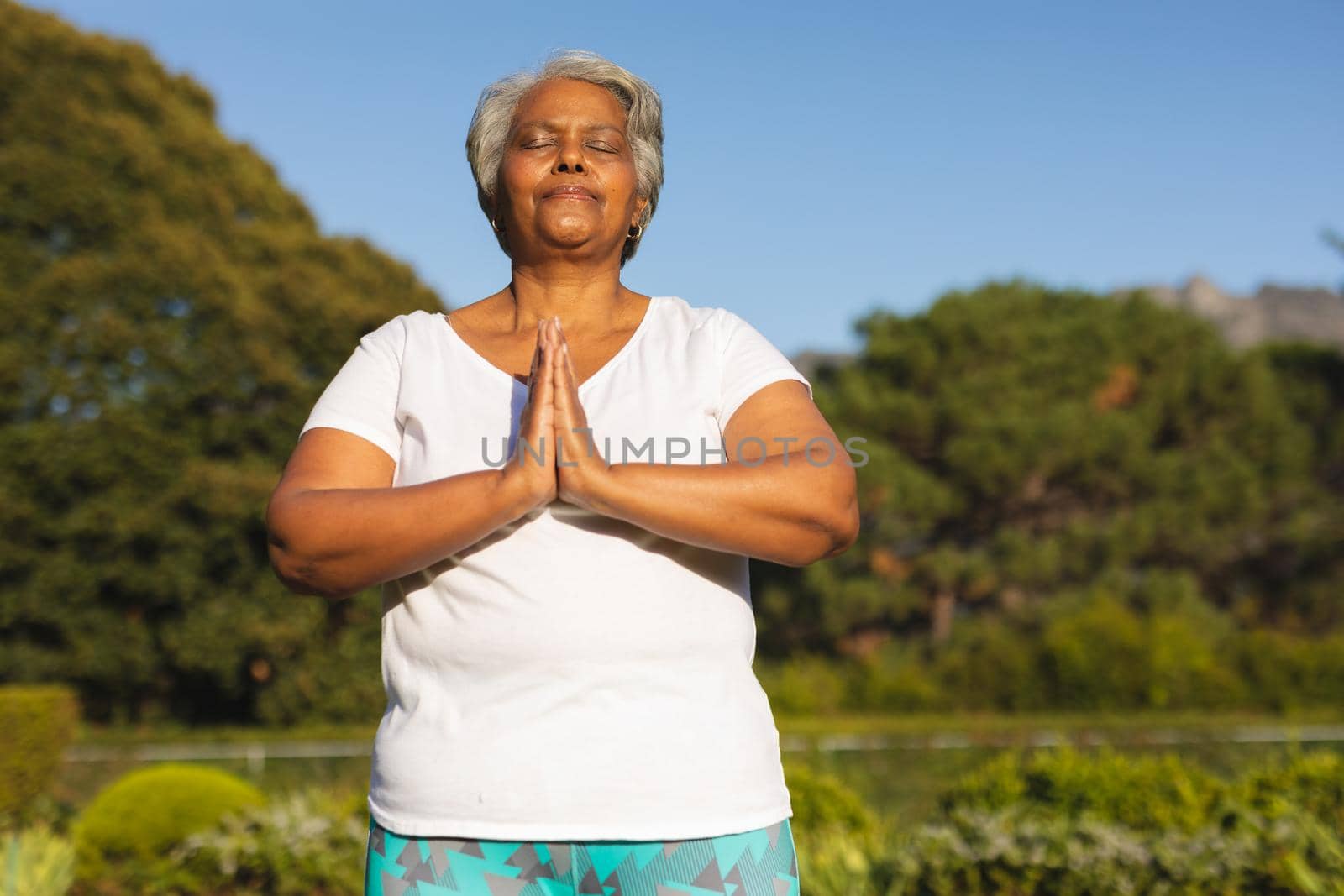 Senior african american woman with eyes closed practicing yoga in stunning countryside. retirement and active senior lifestyle concept.