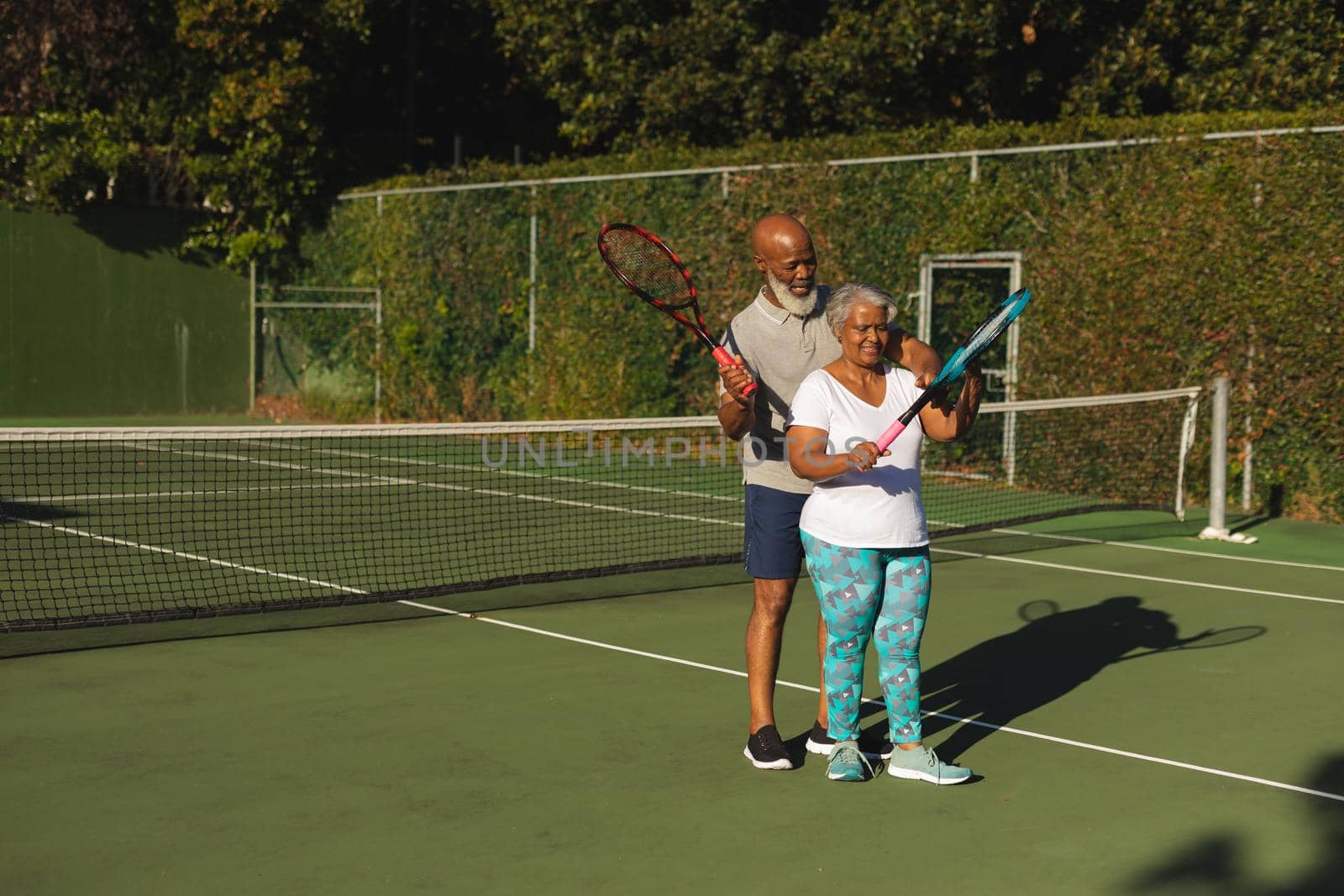 Portrait of smiling senior african american couple with tennis rackets on tennis court. retirement and active senior lifestyle concept.