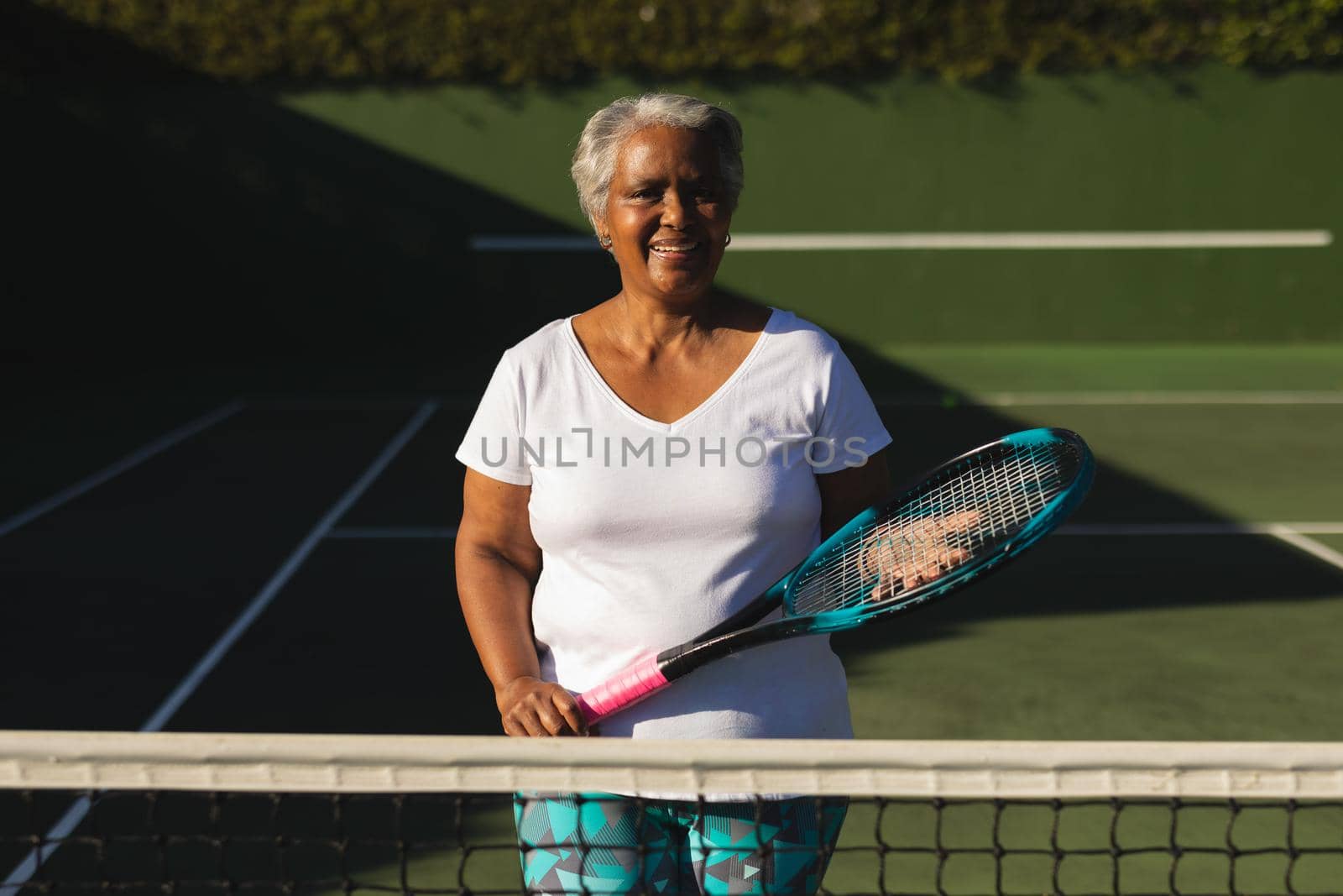 Portrait of smiling senior african american woman holding tennis racket on tennis court. retirement and active senior lifestyle concept.