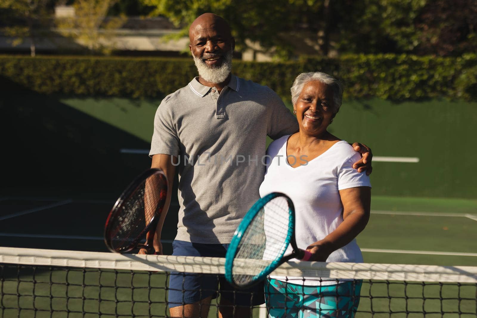 Portrait of smiling senior african american couple with tennis rackets on tennis court by Wavebreakmedia