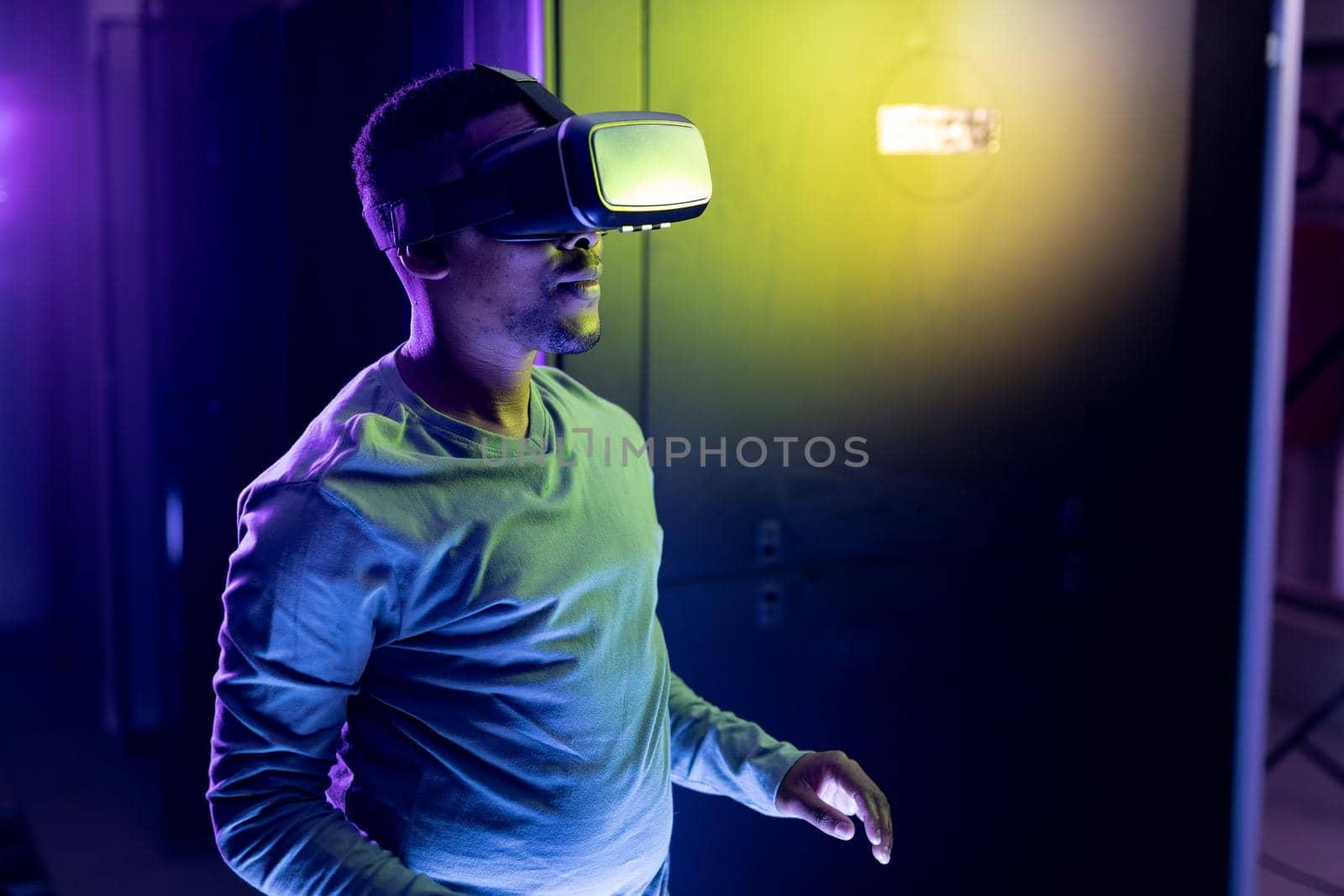 African american male computer technician wearing vr headset and working in server room. digital information storage and communication network technology.