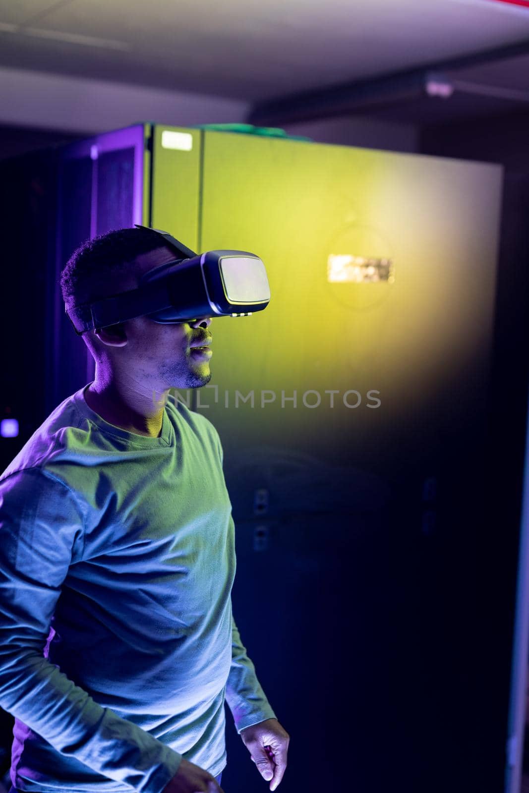 African american male computer technician wearing vr headset and working in server room. digital information storage and communication network technology.