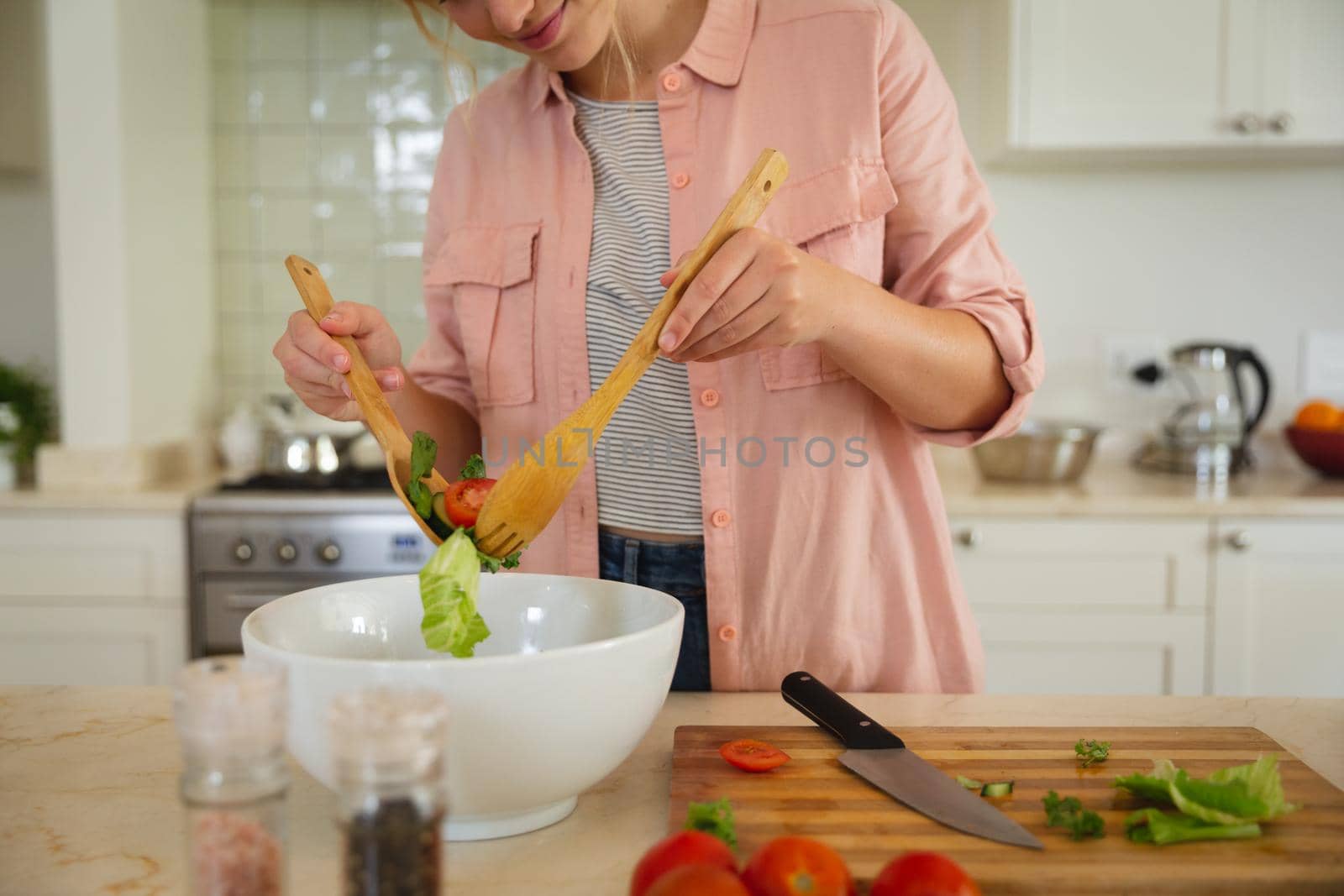 Happy caucasian woman standing in kitchen preparing food, tossing salad and smiling. spending free time at home.