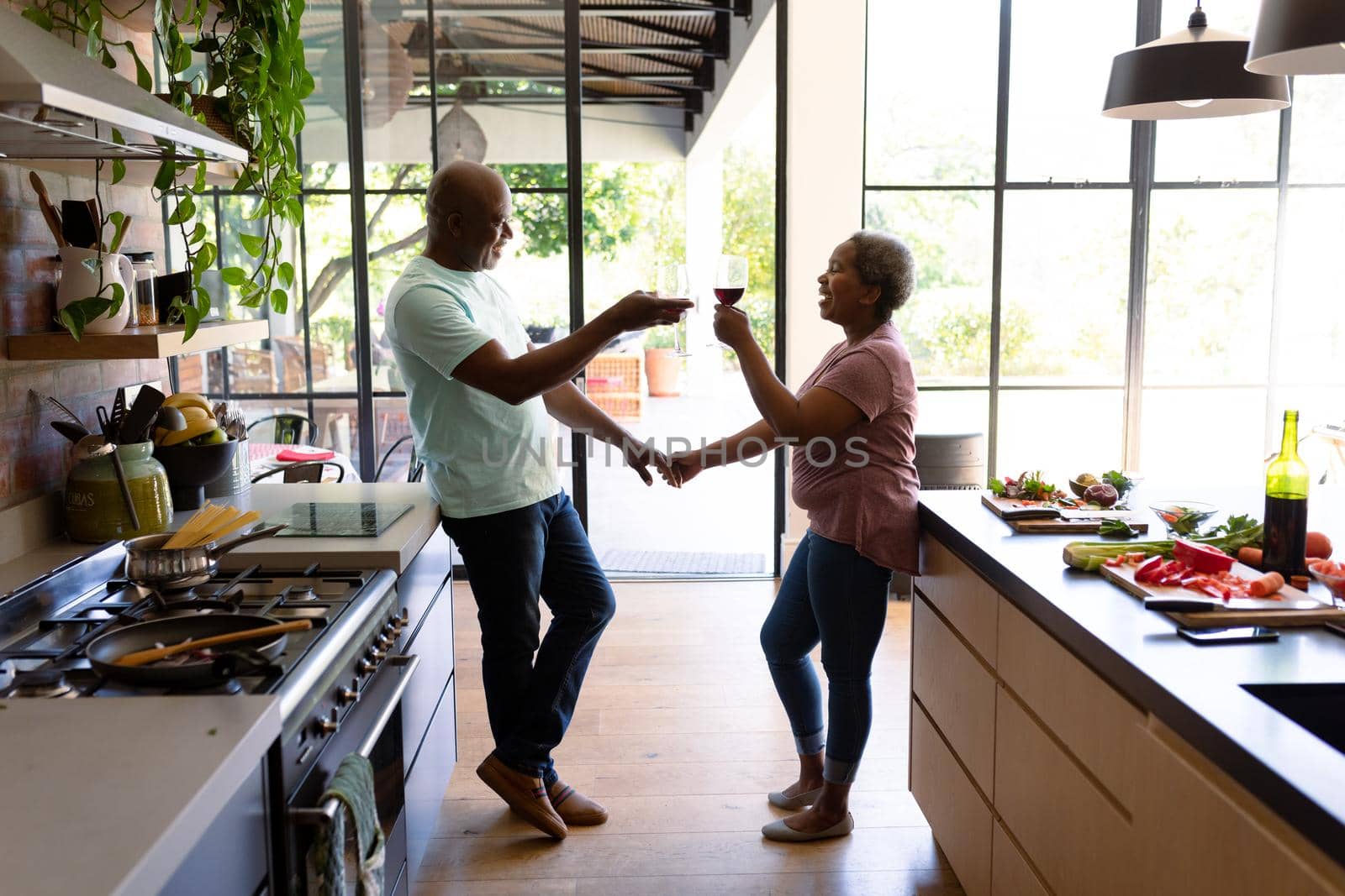 Happy african american senior drinking wine together in kitchen. retirement lifestyle, leisure and spending time at home.