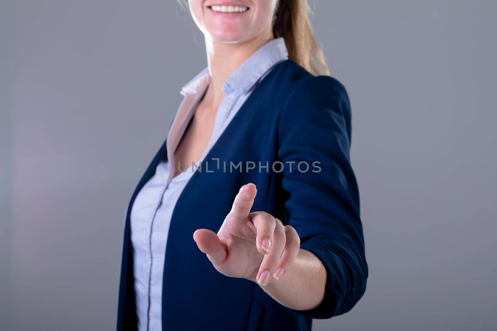 Smiling caucasian businesswoman touching virtual interface, isolated on grey background. business technology, communication and growth concept digitally generated composite image.