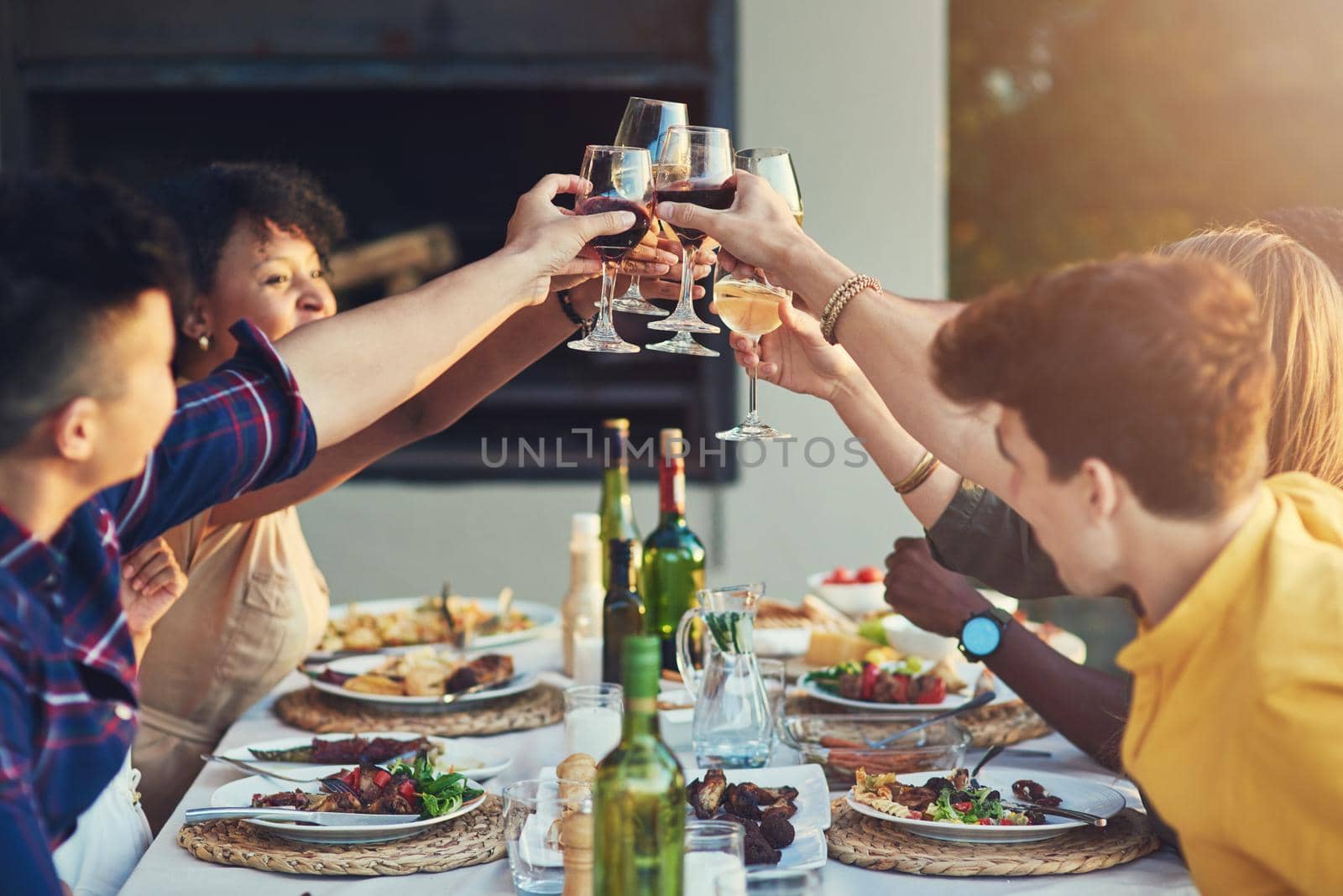 Sharing a toast with the best company in the world. Shot of a group of friends raising up their glasses for a toast while sitting around a table together outdoors. by YuriArcurs