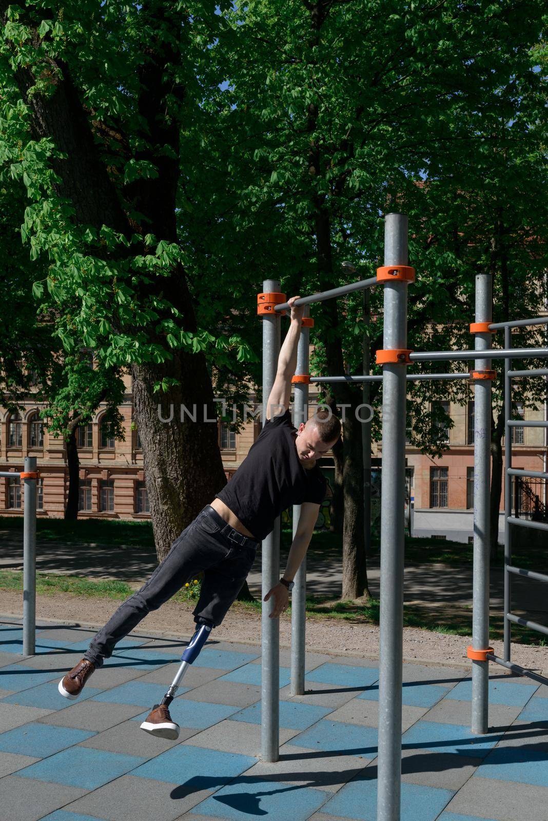 athletic young man with artificial leg working out on a bars. Outdoors