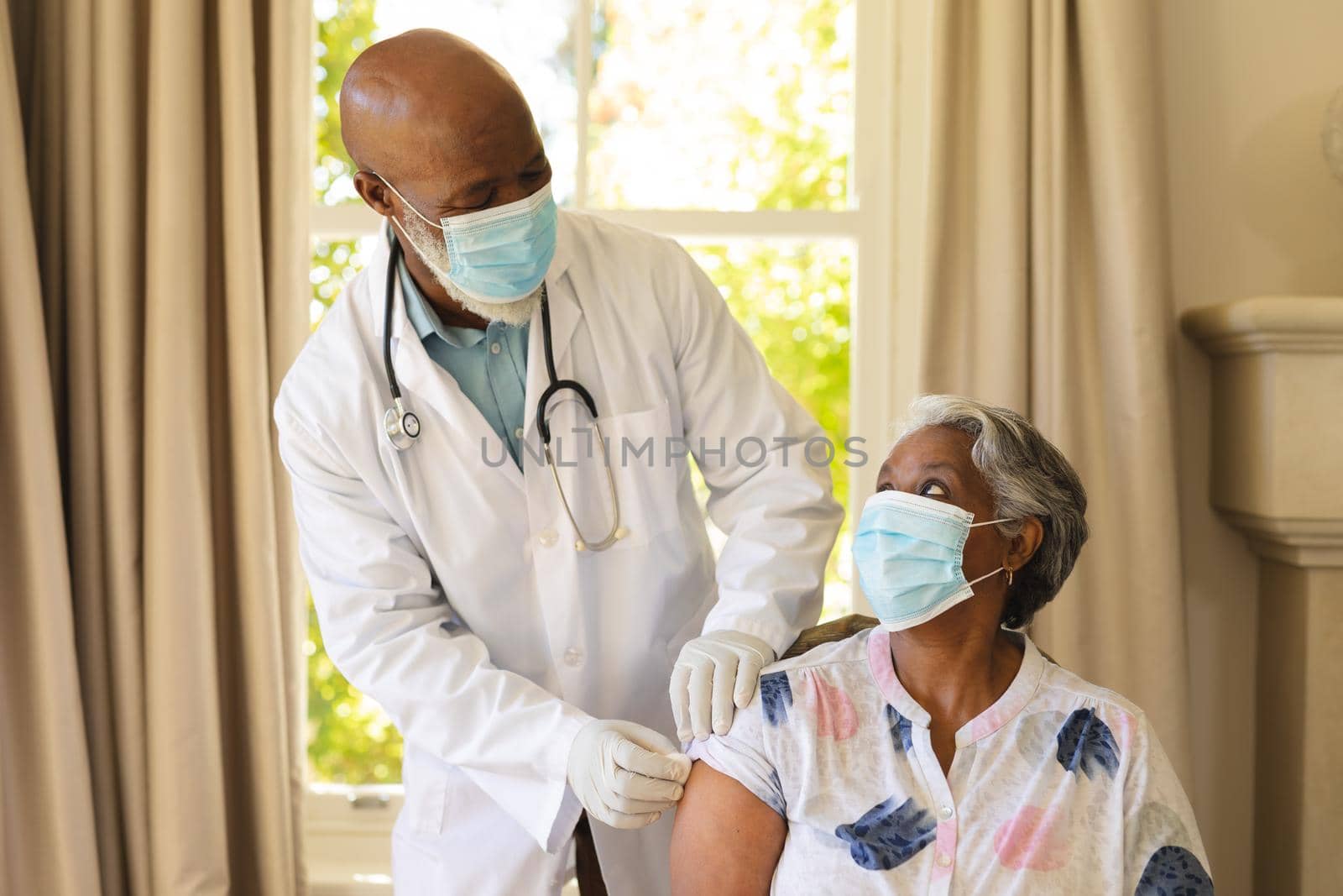 Senior african american woman and male doctor in face masks, woman receiving vaccination. retirement and senior lifestyle during covid 19 pandemic concept.