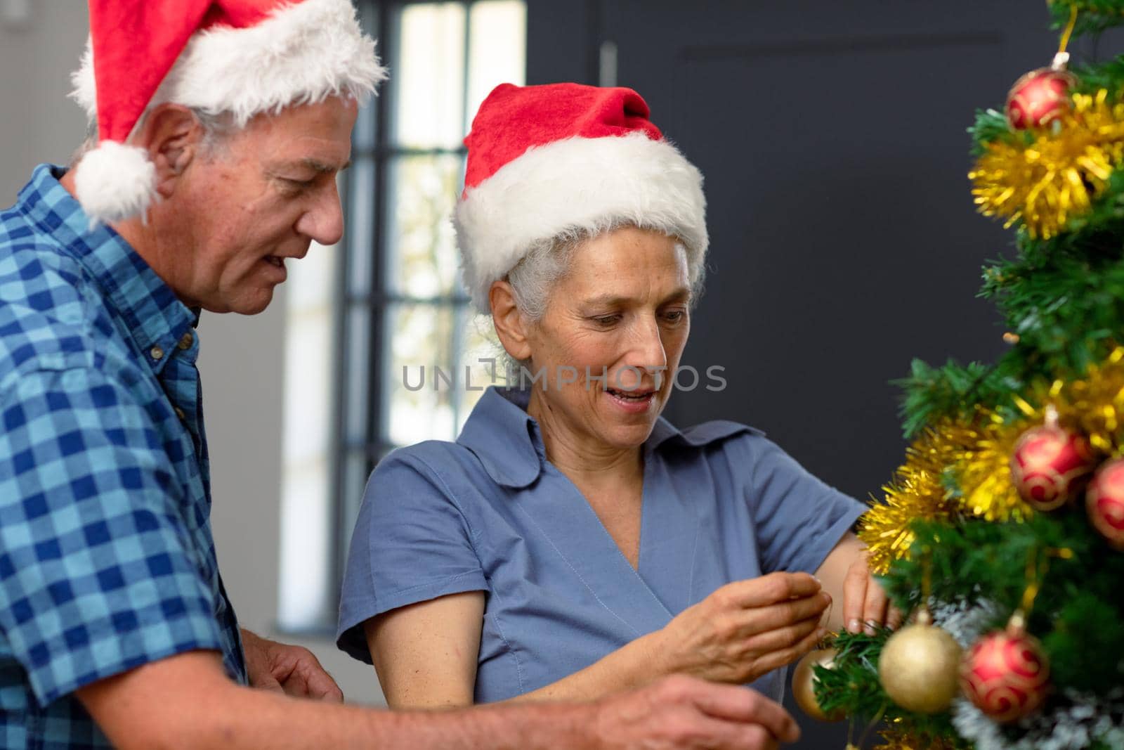 Happy caucasian senior couple wearing santa hat, decorating christmas tree. christmas, festivity and tradition at home.
