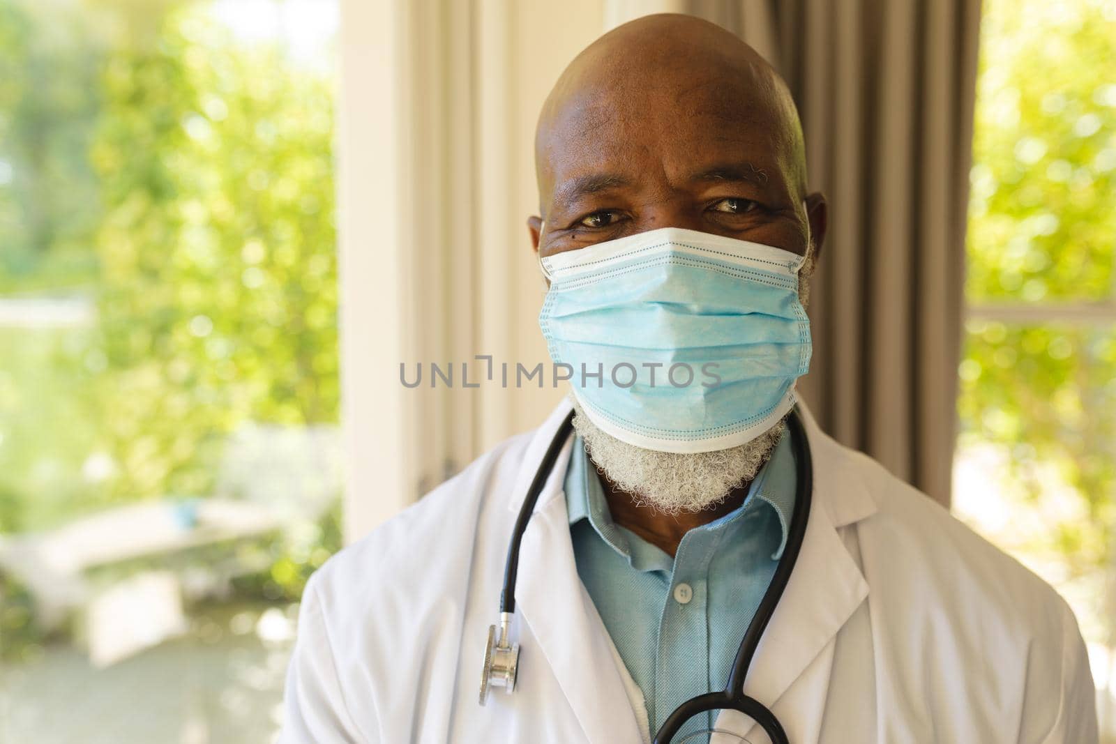 Portrait of senior african american male doctor in face mask and lab coat by Wavebreakmedia