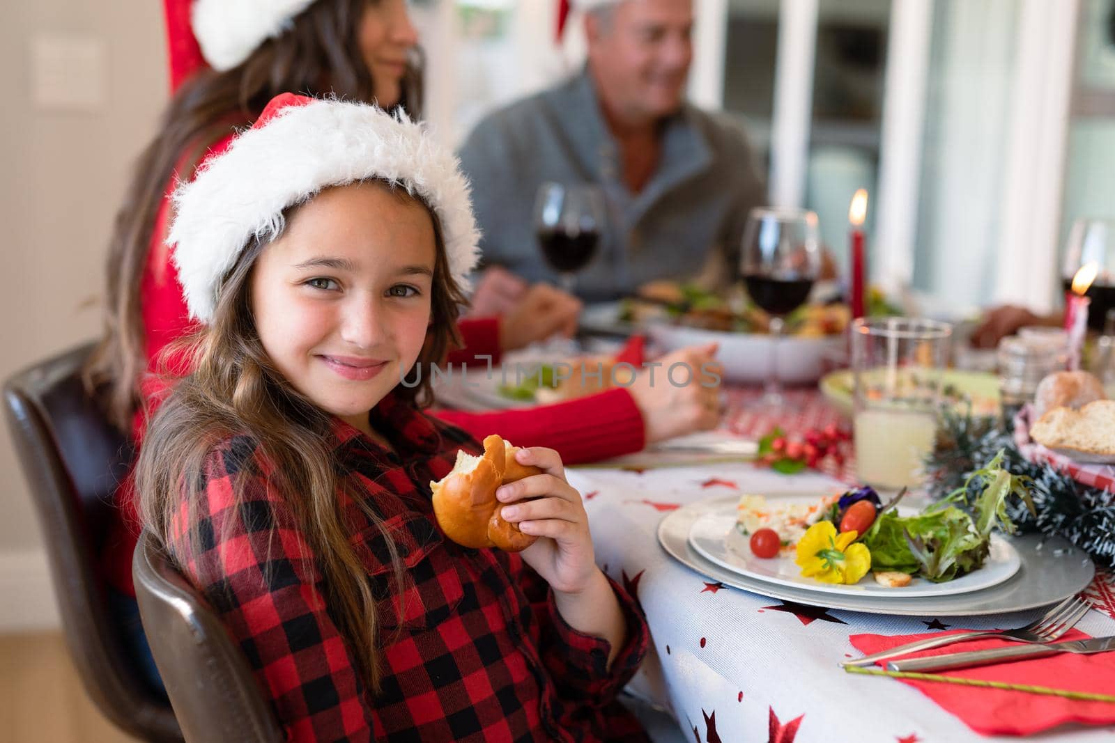 Happy caucasian girl wearing santa hats sitting at christmas table and looking at camera. family christmas time and festivity together at home.