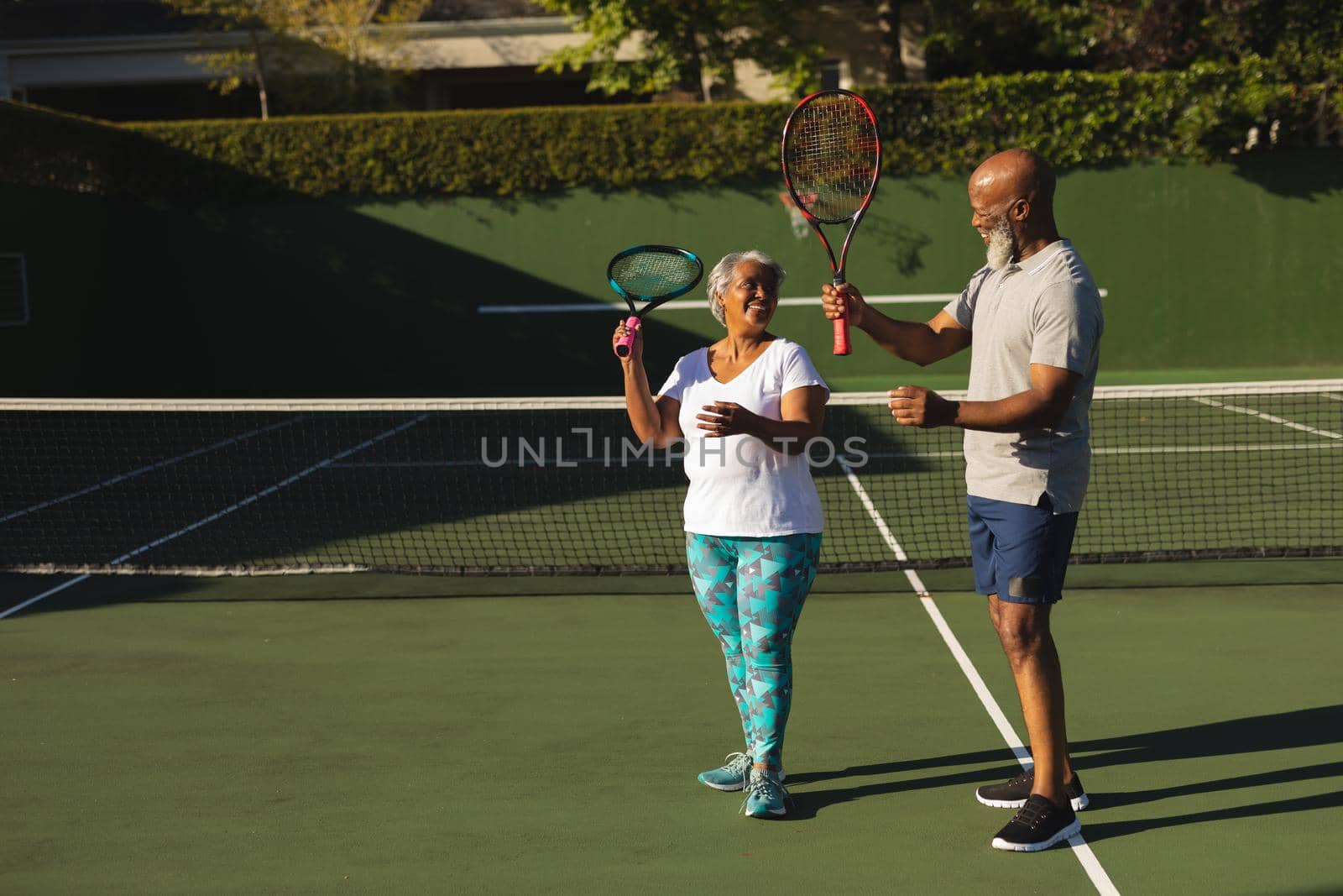 Portrait of smiling senior african american couple with tennis rackets on tennis court. retirement and active senior lifestyle concept.