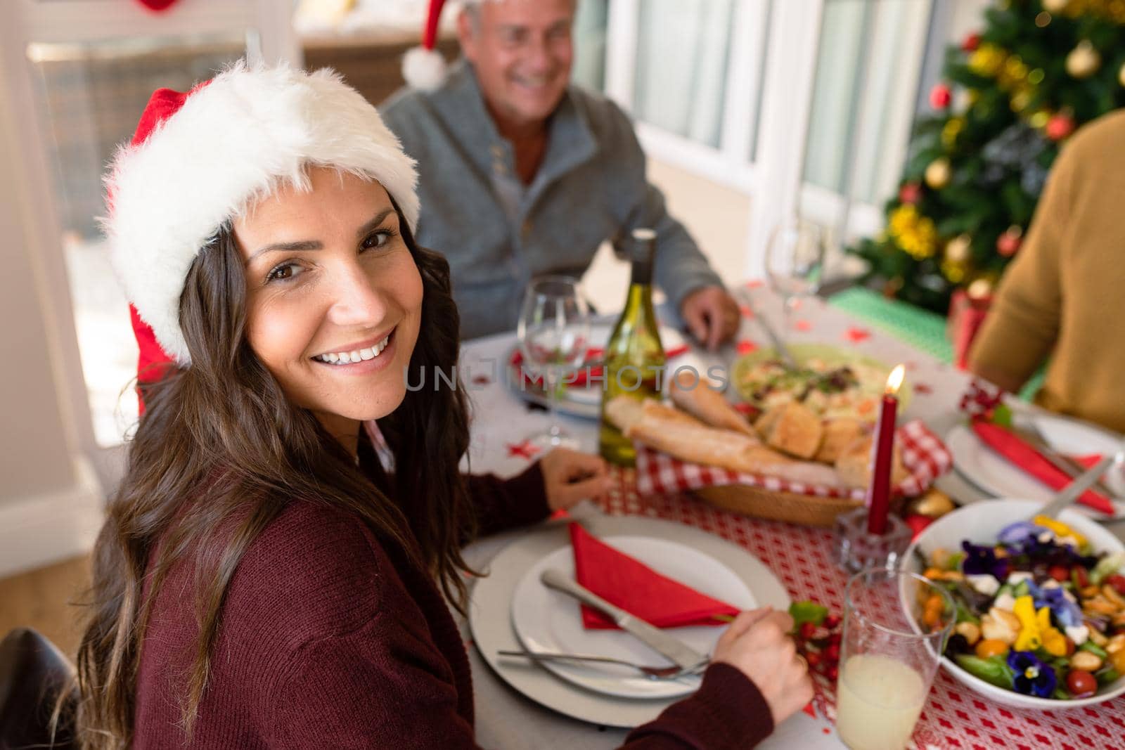 Happy caucasian woman wearing santa hat sitting at christmas table and looking at camera. family christmas time and festivity together at home.