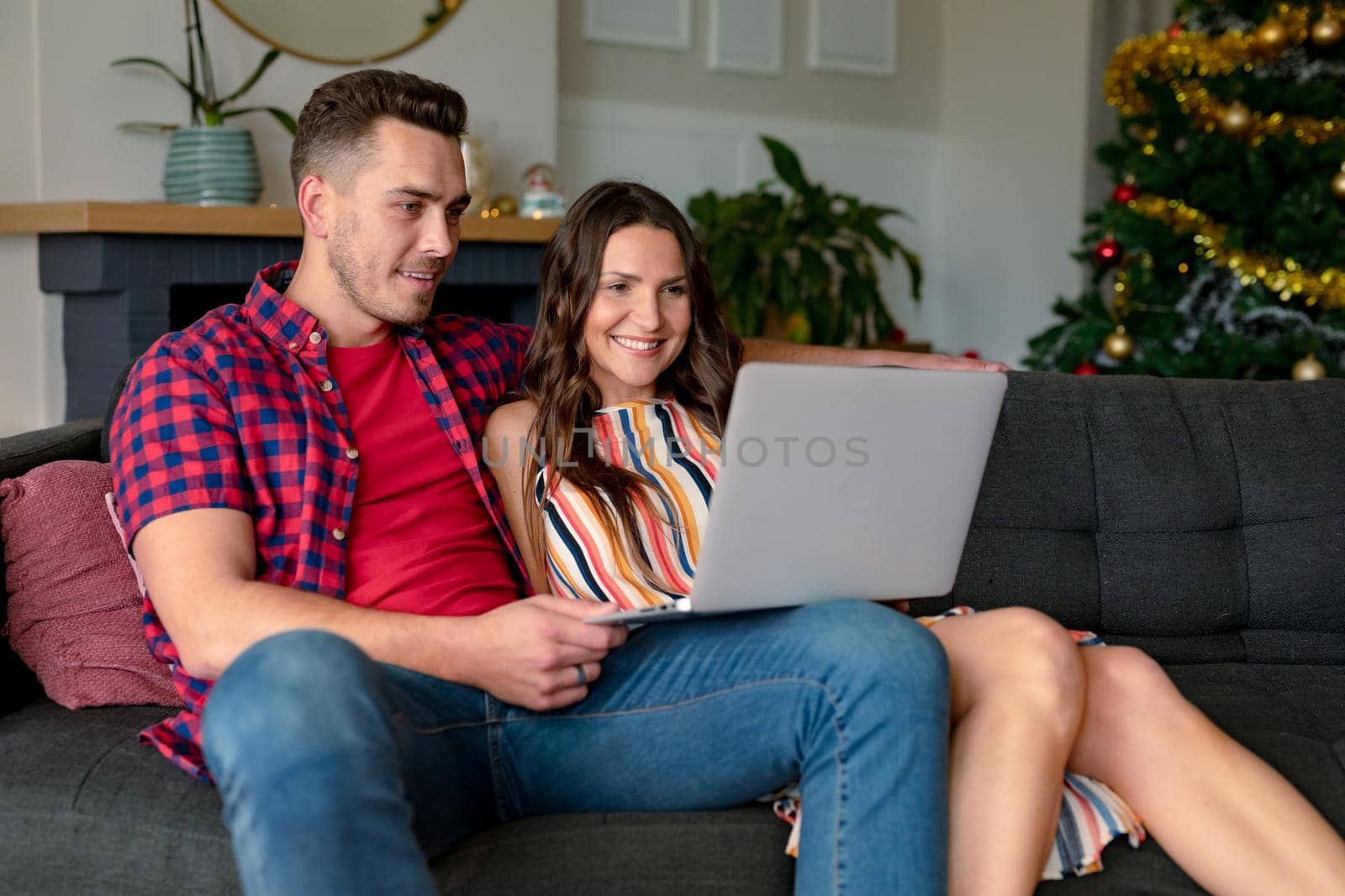 Happy caucasian couple sitting on sofa and having video call on laptop at christmas time by Wavebreakmedia
