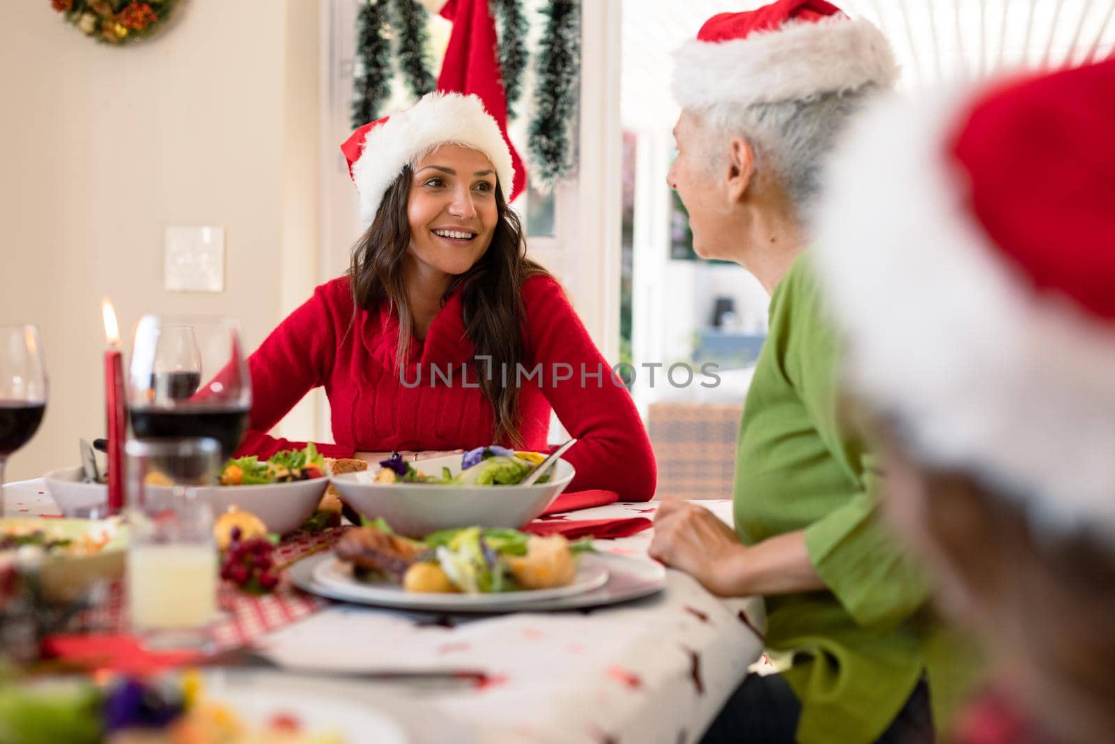 Happy caucasian adult daughter and senior mother wearing santa hats talking at christmas table by Wavebreakmedia