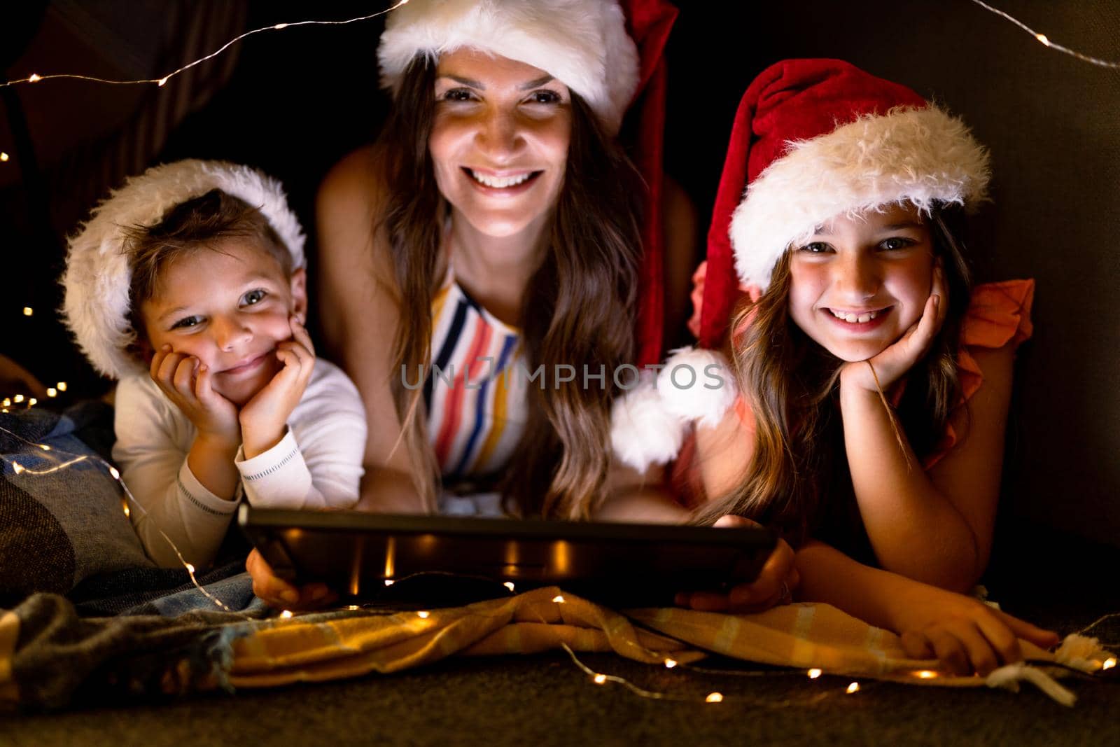 Happy caucasian mother, daughter and son wearing santa hats, using tablet at christmas time by Wavebreakmedia