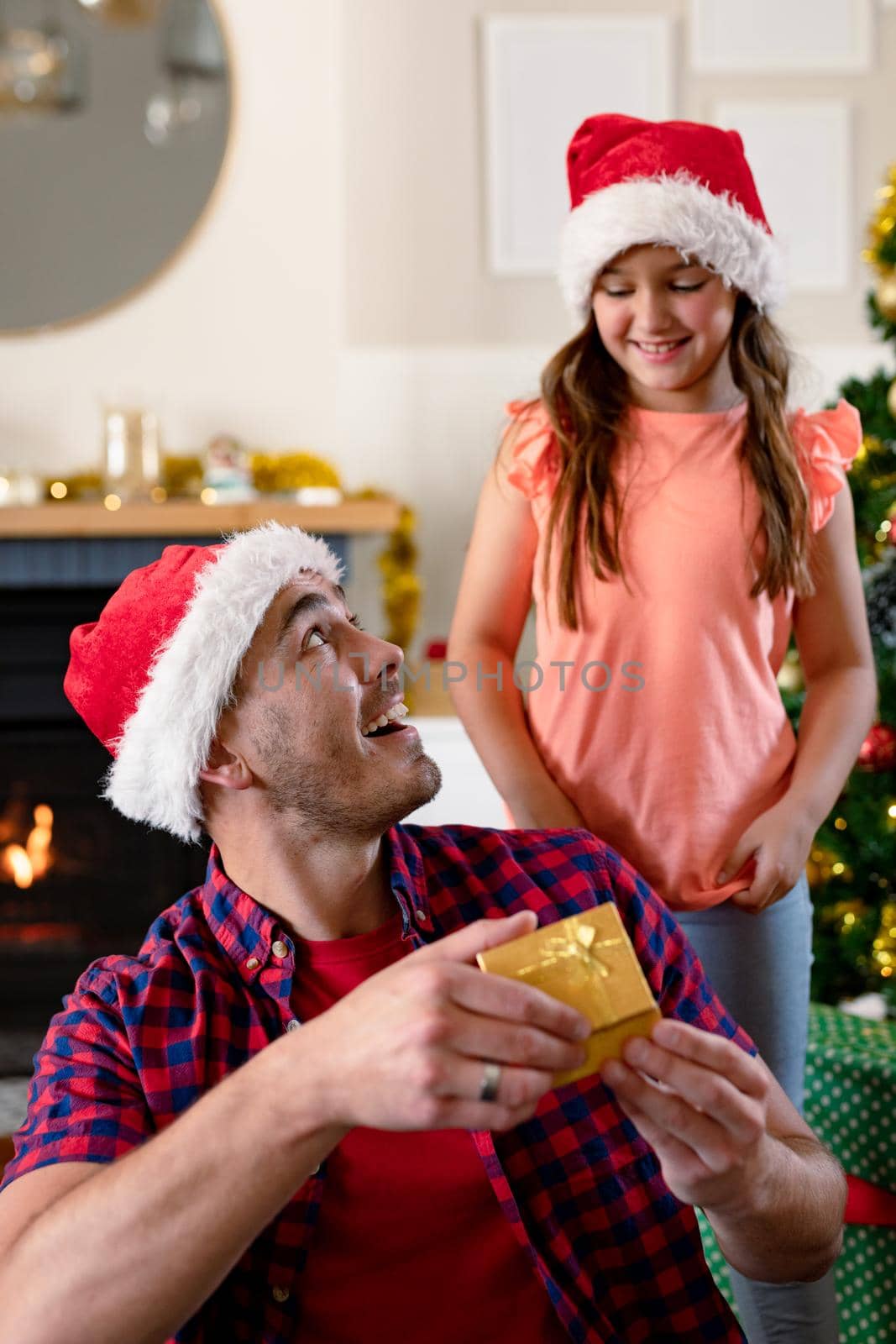 Surprised caucasian father wearing santa hat receiving present from his daughter at christmas time. family christmas time and festivity together at home.