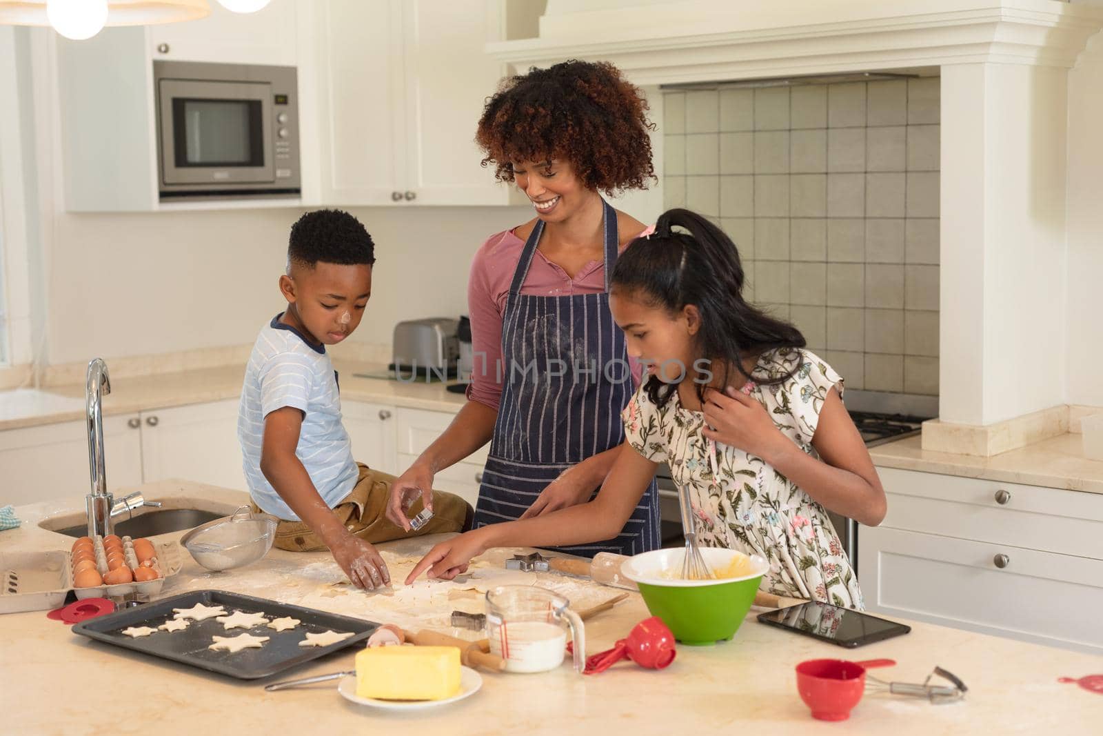 Happy african american mother with son and daughter baking in kitchen, cutting cookies. family enjoying quality free time together.