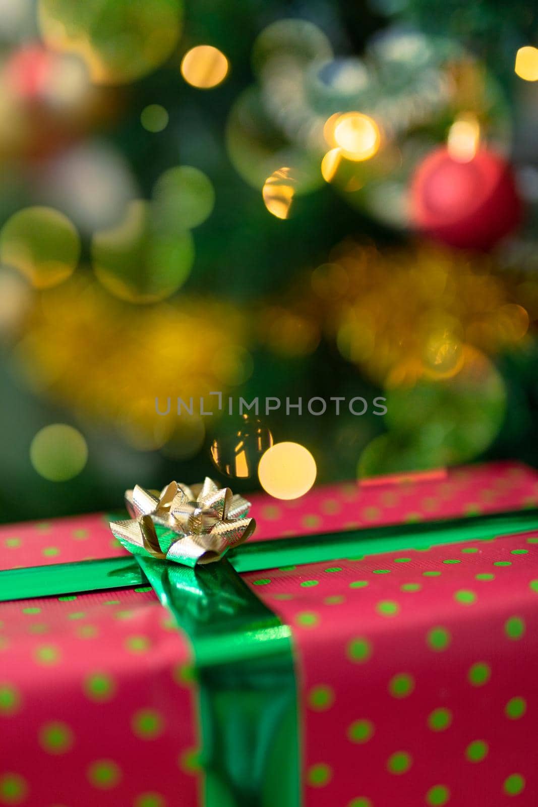 Christmas present in red paper with gold ribbon standing over christmas tree. christmas festivities, traditions and celebrating at home.